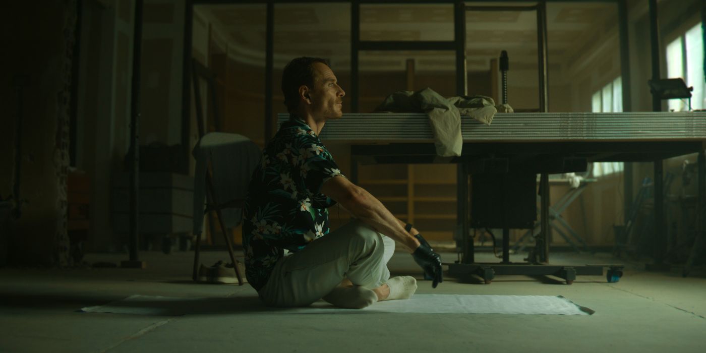Michael Fassbender as The Killer sitting on the floor looking ahead in The Killer