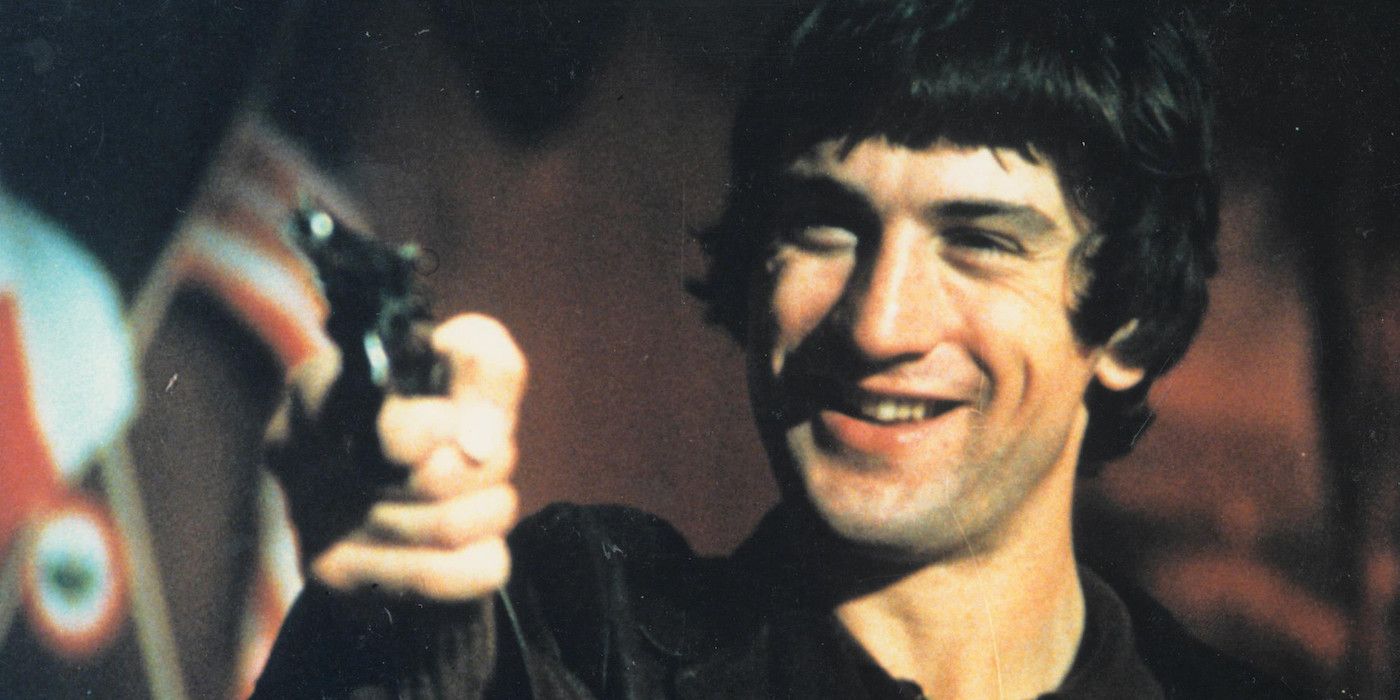 Robert De Niro smiling and pointing a gun at someone off screen in Mean Streets (1973)