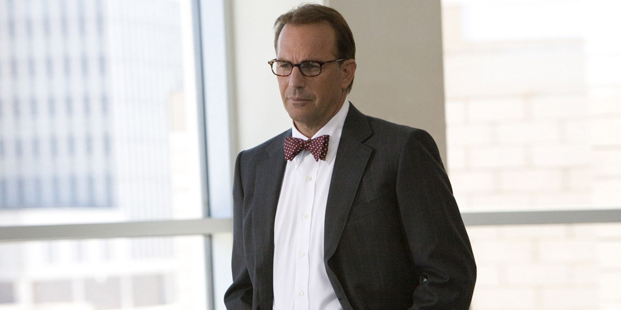 Kevin Costner as Earl Brooks/The Thumbprint Killer, wearing a suit and glasses, standing in a room with lots of windows in Mr. Brooks
