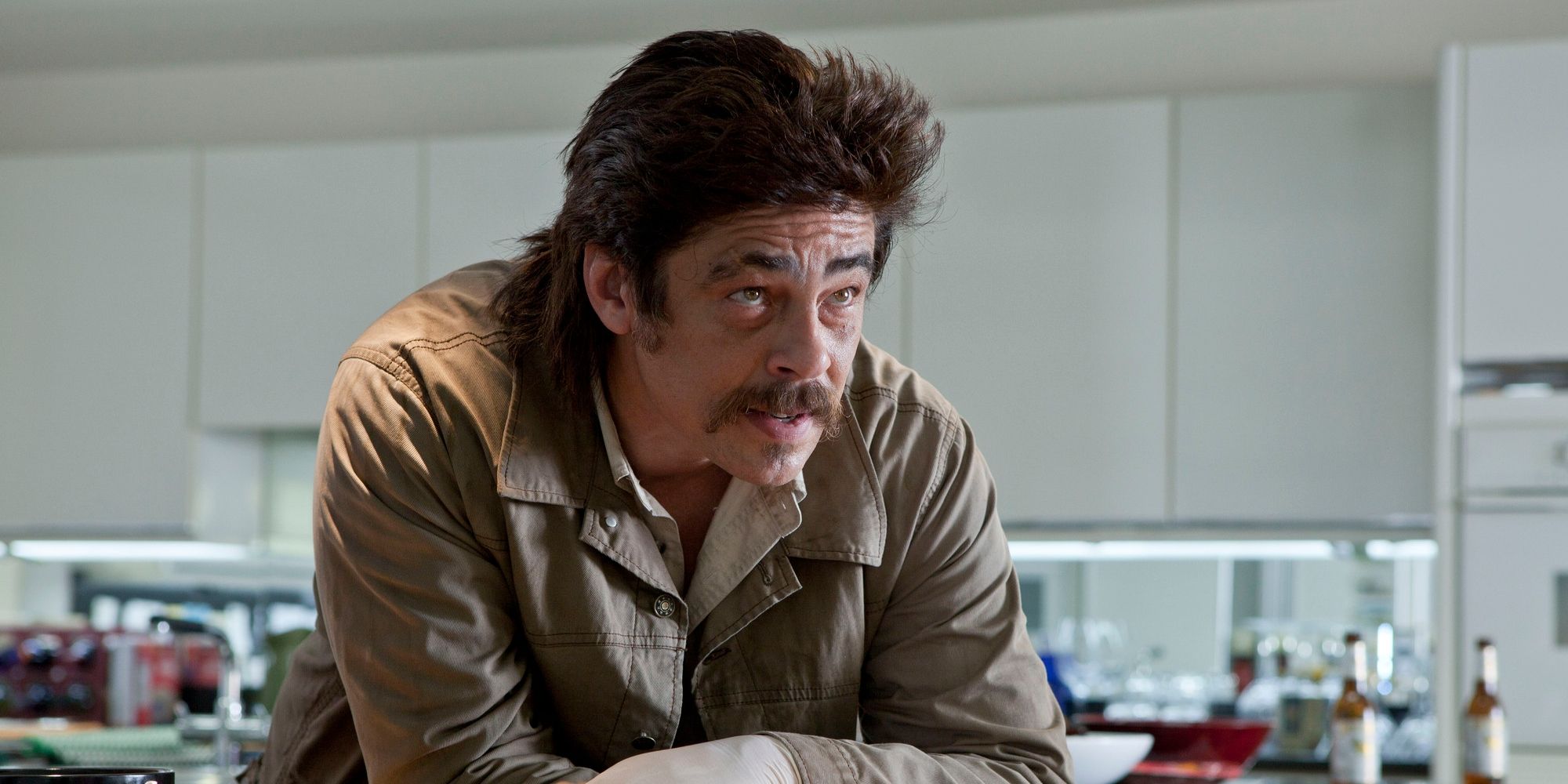 Benicio Del Toro as Lado leaning over a counter and looking ahead in Savages
