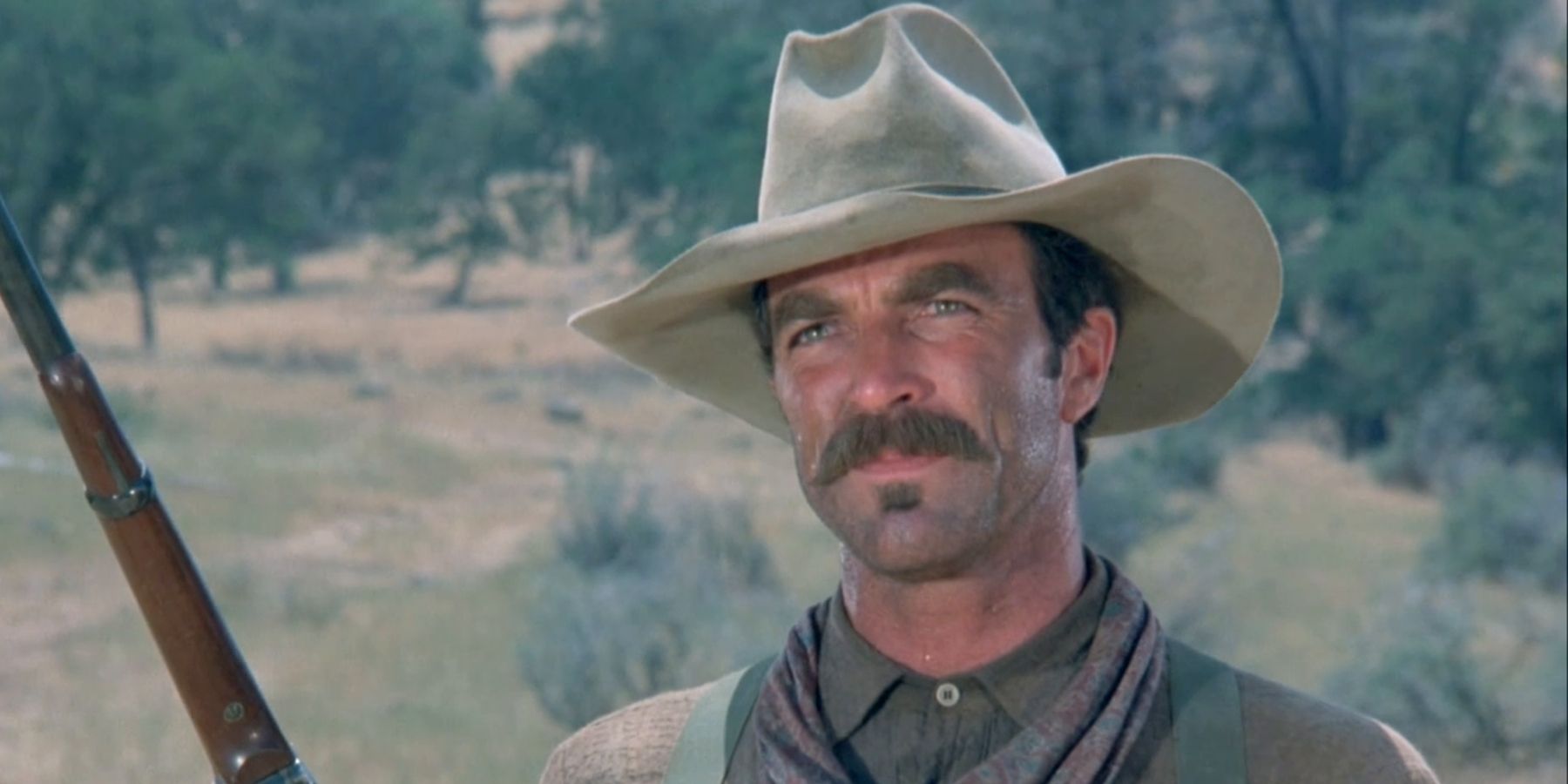 Tom Selleck as Mac Traven, standing outside, wearing a stetson and holding a rifle in The Shadow Riders