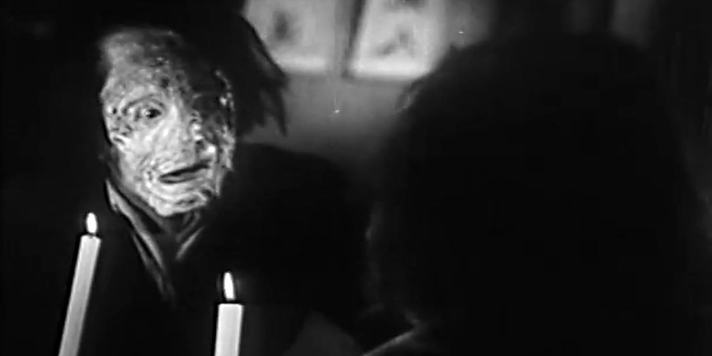 The disfigured character looks at himself in a mirror with a candle in Song at Midnight.