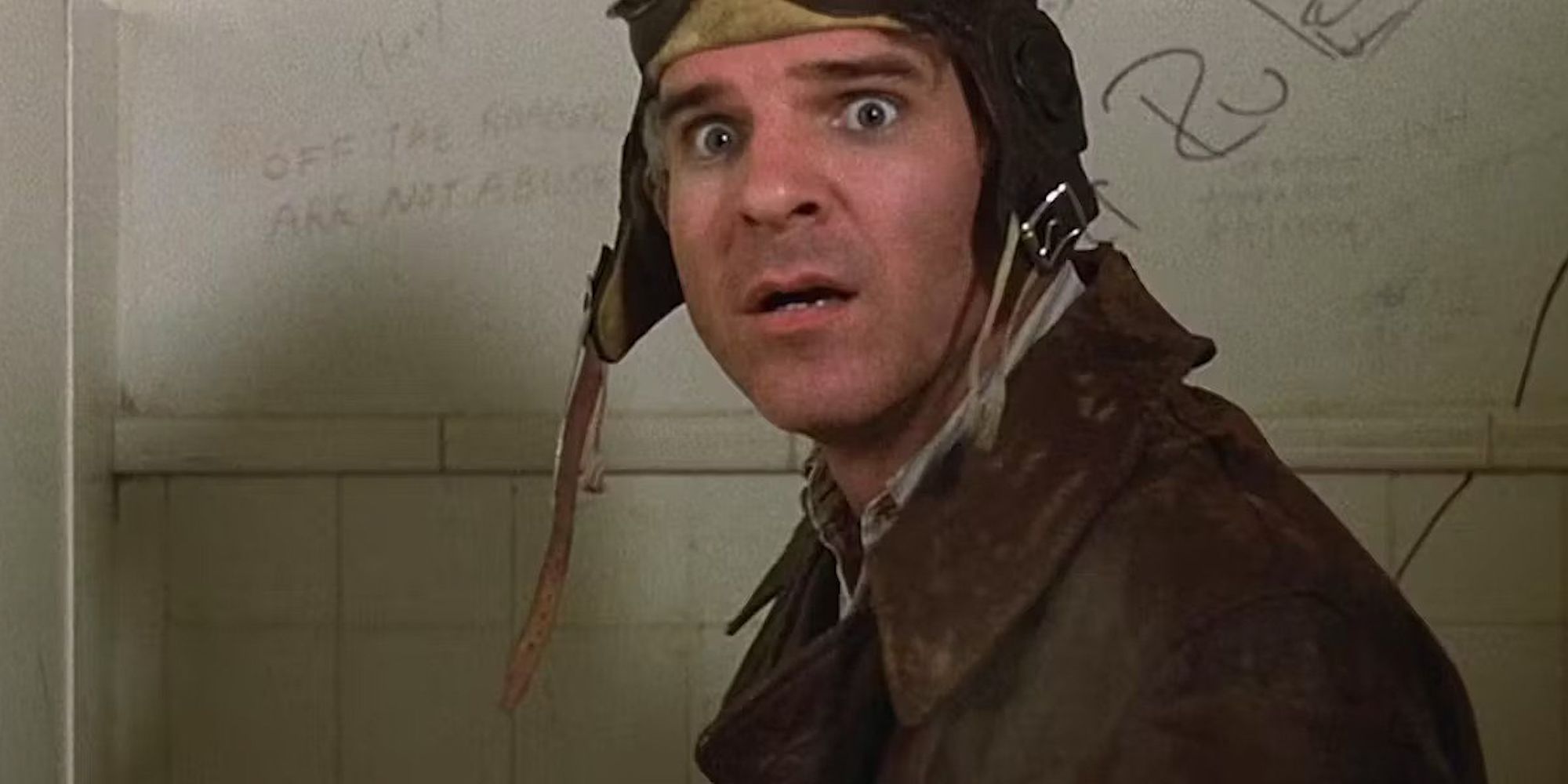 Navin Johnson (Steve Martin) stands in a toilet cubicle with an aviator cap on as he looks to someone shocked.