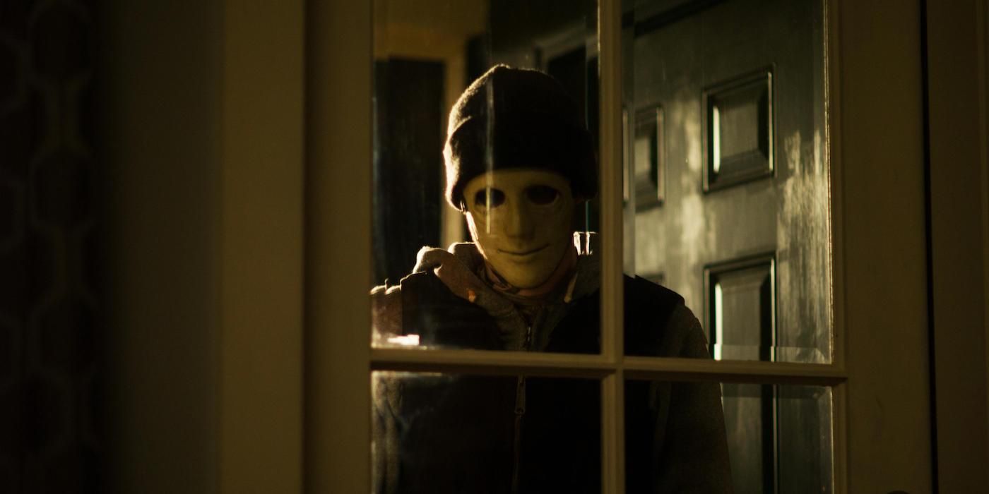 The Man (John Gallagher Jr.) stands at window wearing a mask in &lsquo;Hush&rsquo;