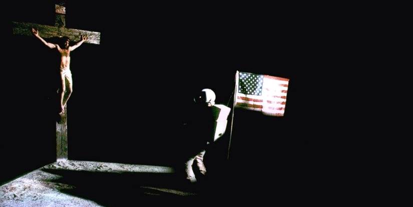 Astronauts, kas devītajā konfigurācijā tur ASV karogu krustā sišanas priekšā