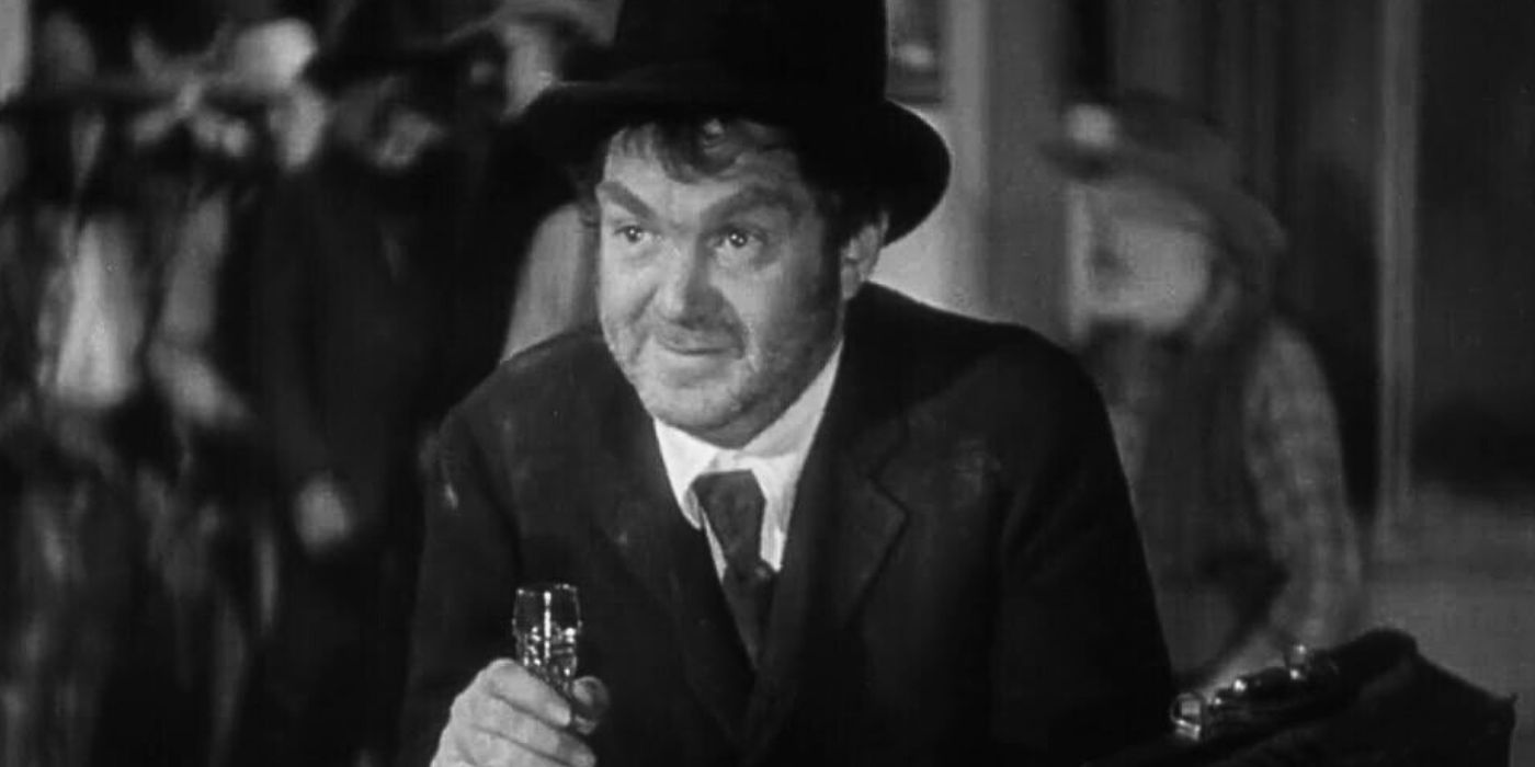 Thomas Mitchell sitting alone at a table with a bottle of whiskey in Stagecoach (1939)