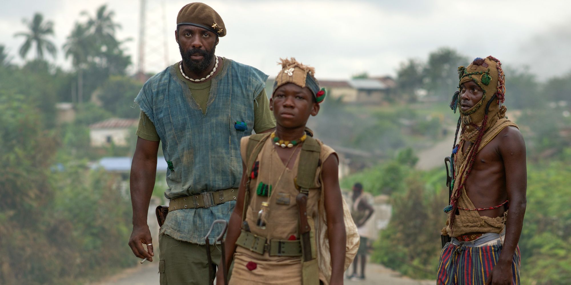 Idris Elba as Commandant and Abraham Attah as Agu stand side-by-side in the middle of the road in Beasts of No Nation