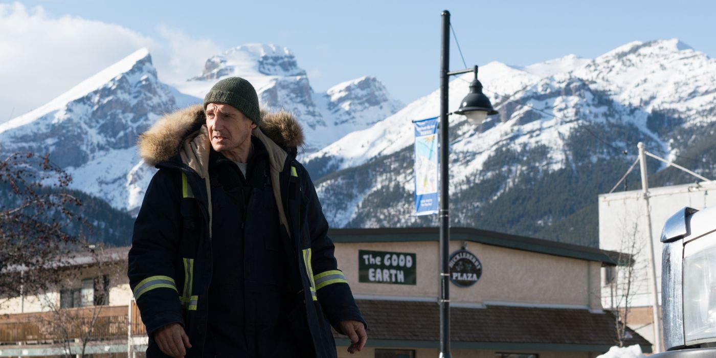Liam Neeson standing in a town in fron of snowy mountains in Cold Pursuit