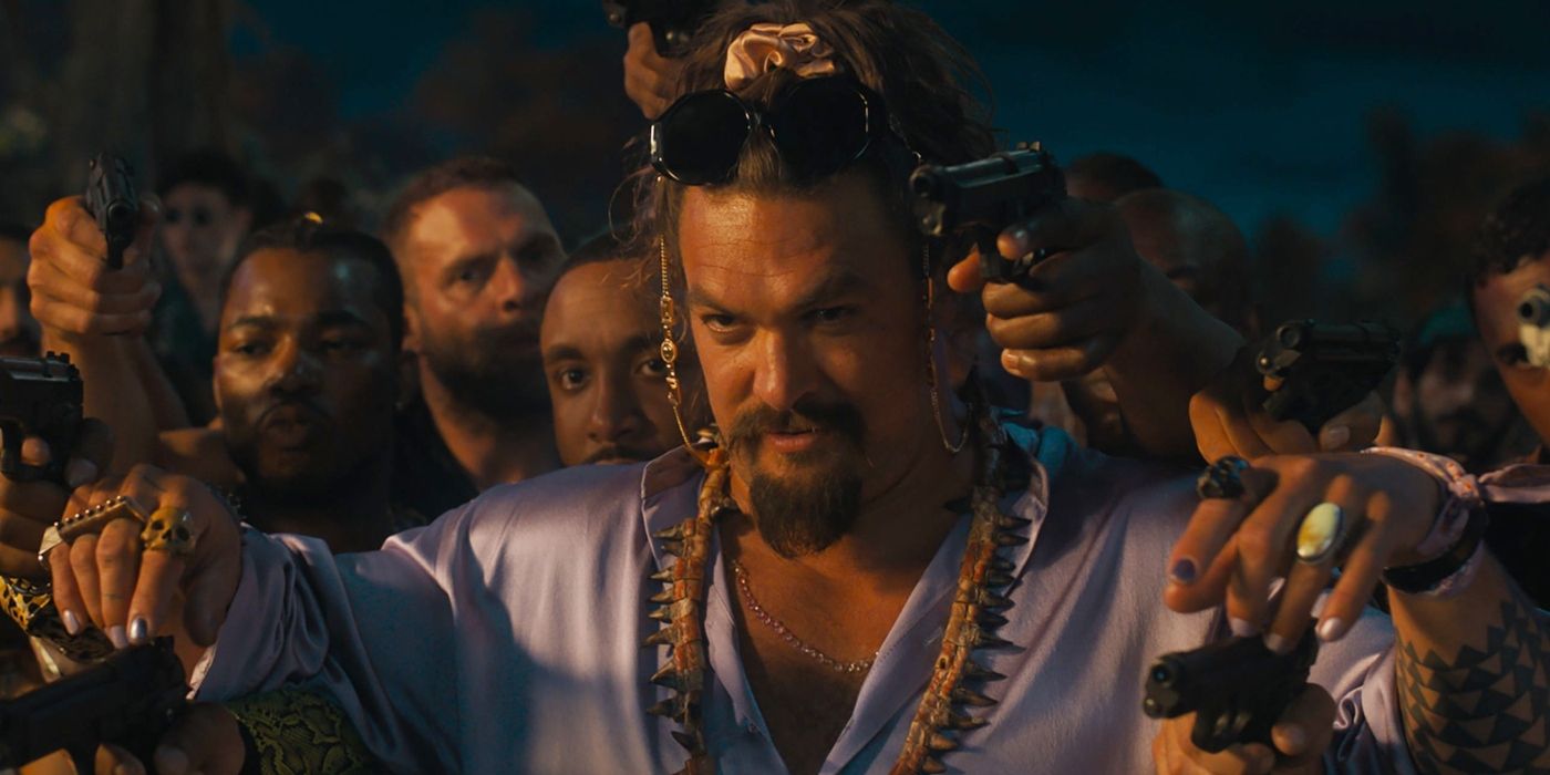 Jason Mamoa as Dante wearing a white shirt and tooth necklace framed by hands holding guns in Fast X.