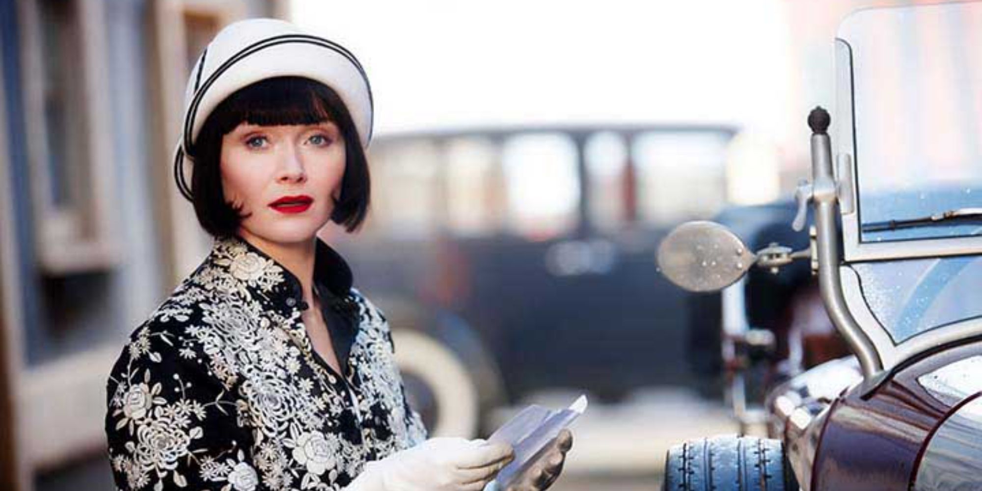 Essie Davis as Phryne Fisher holding a piece of paper and looking in the distance in Miss Fisher's Murder Mysteries