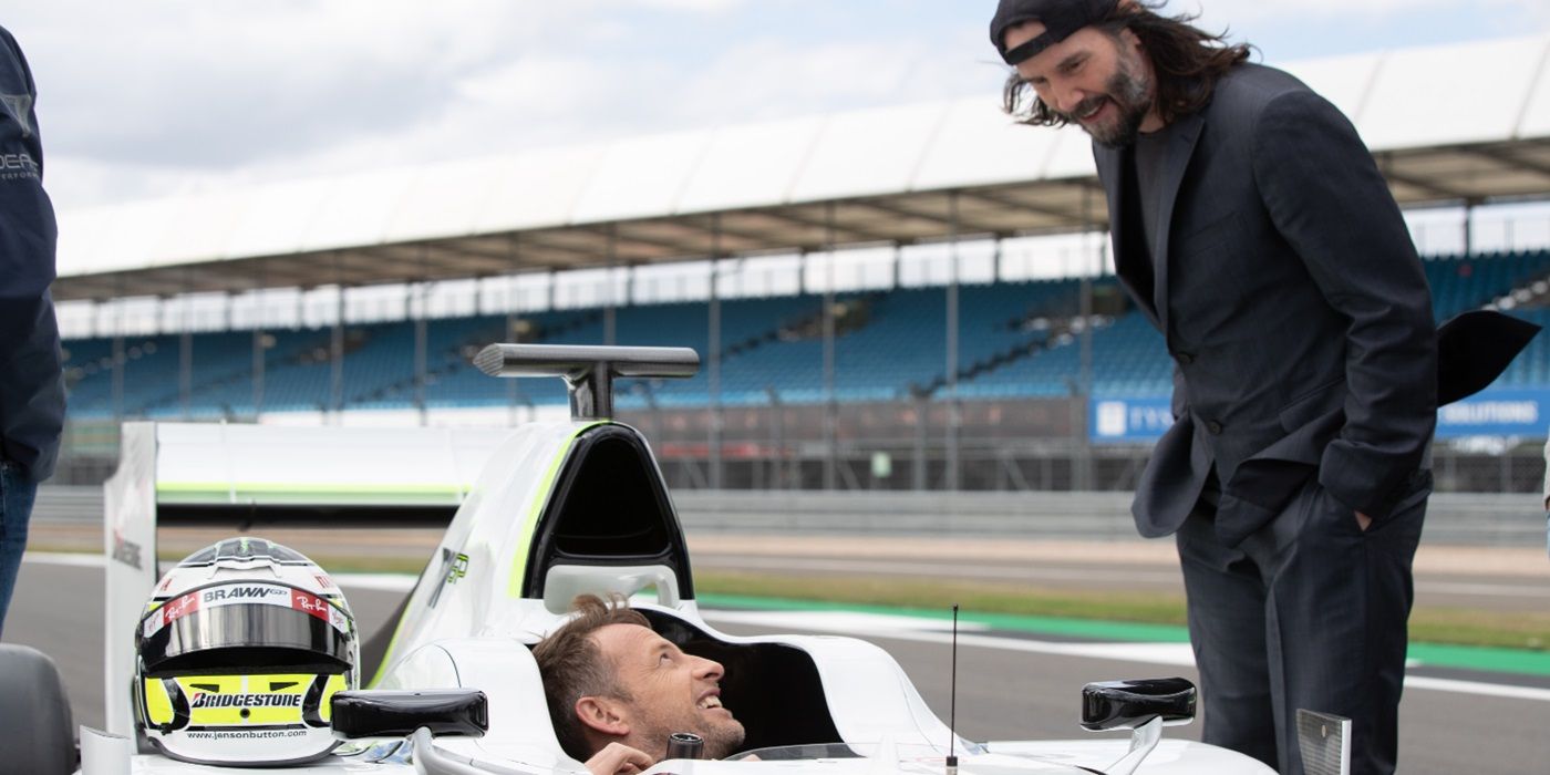 Keanu Reeves approaching Jenson Button in a race car on the track in Brawn: The Impossible Formula 1 Story