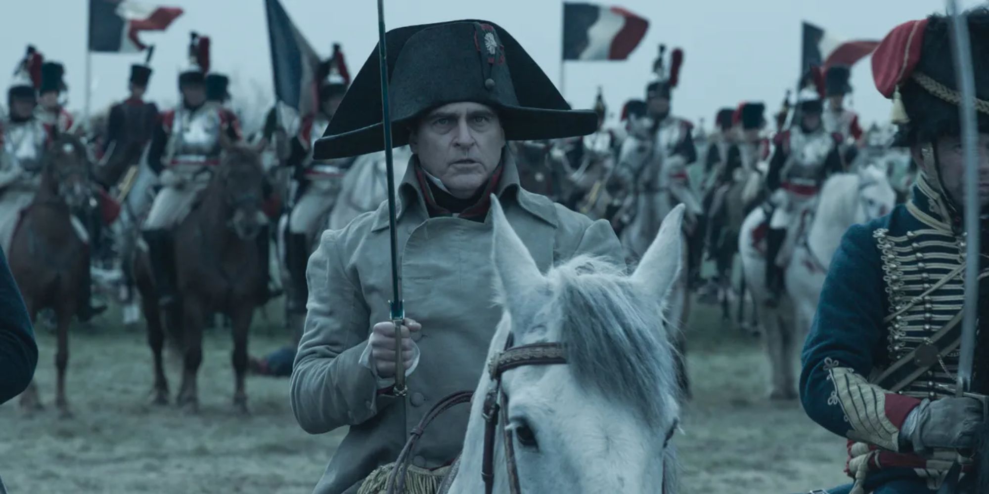 Joaquin Phoenix as Napoleon Bonaparte riding a white horse into battle in Ridley Scott's Napoleon