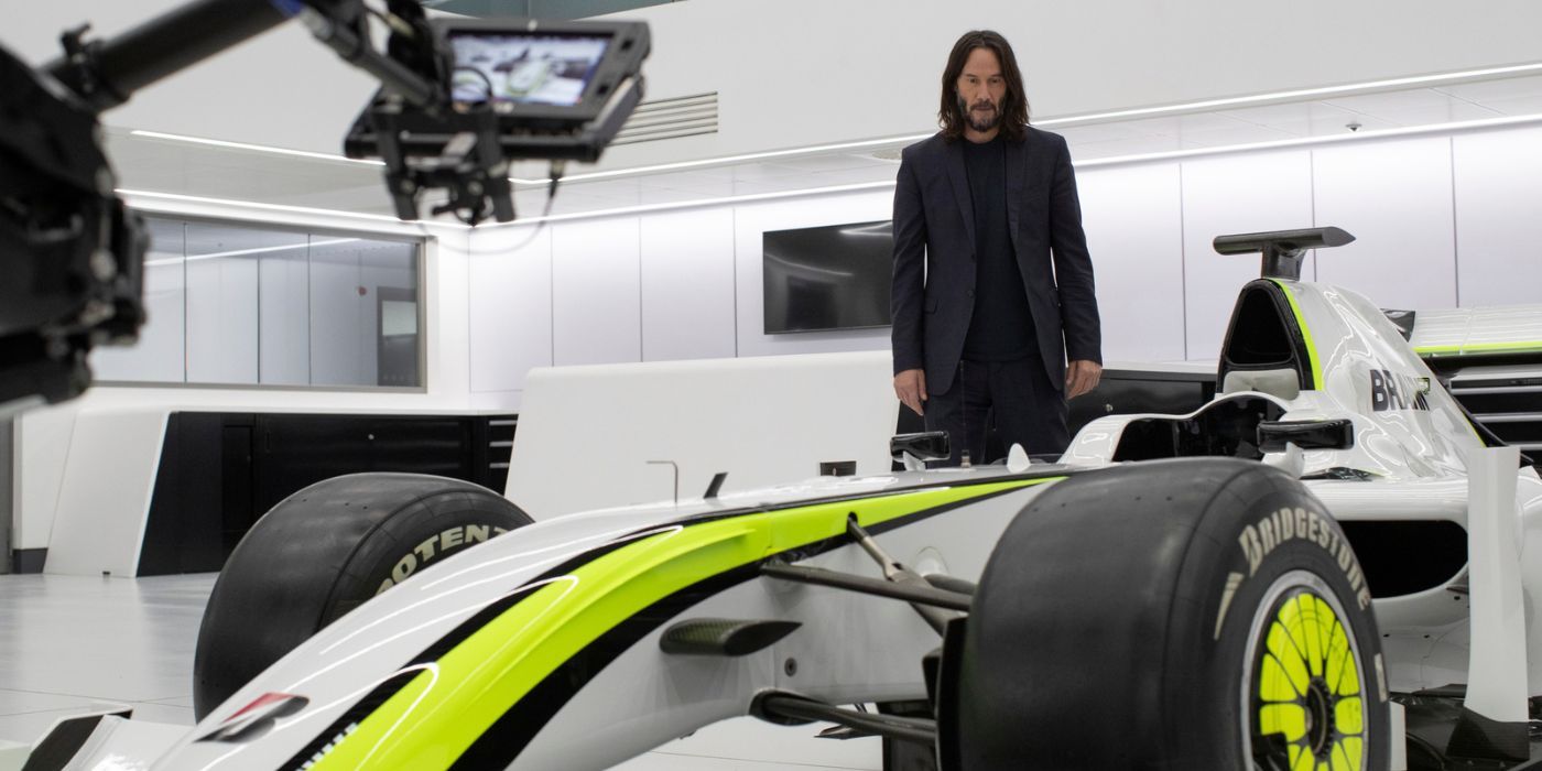 Keanu Reeves stands next to Formula 1 car while filming  'Brawn The Impossible Formula 1 Story'