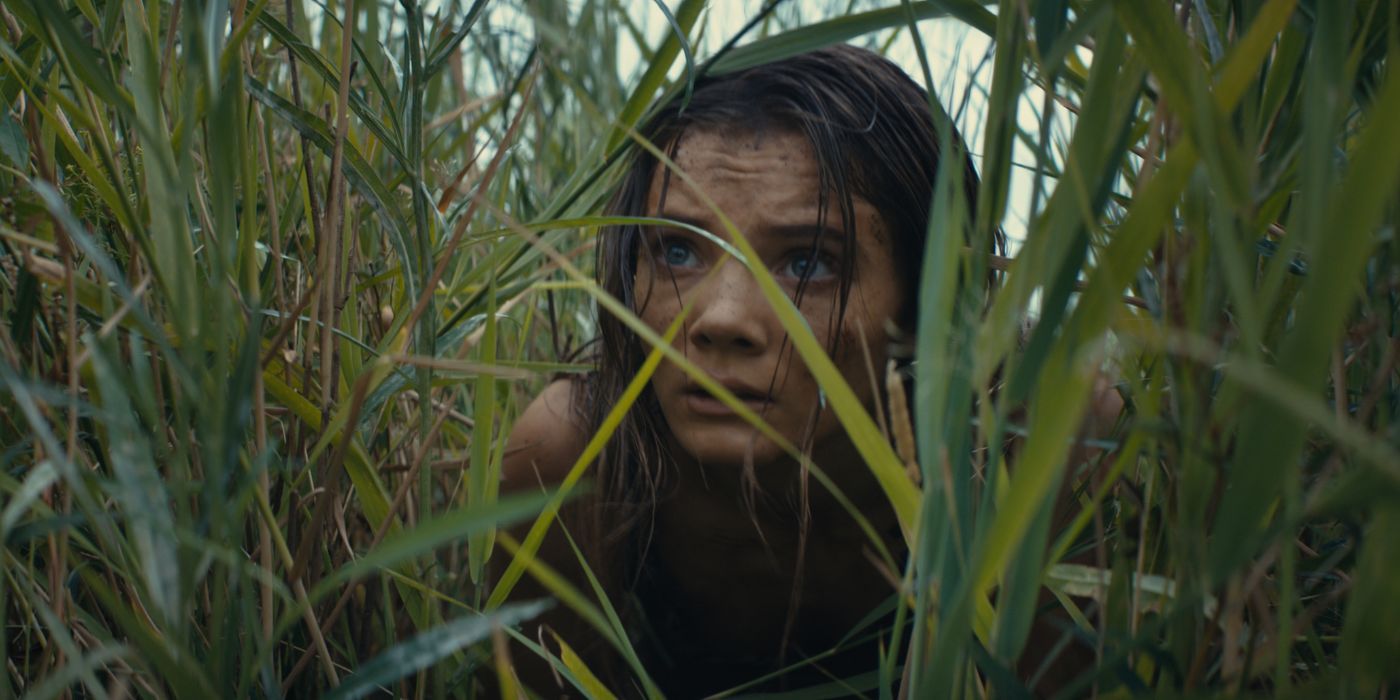 Freya Allan in Kingdom of the Planet of the Apes peering through tall grass