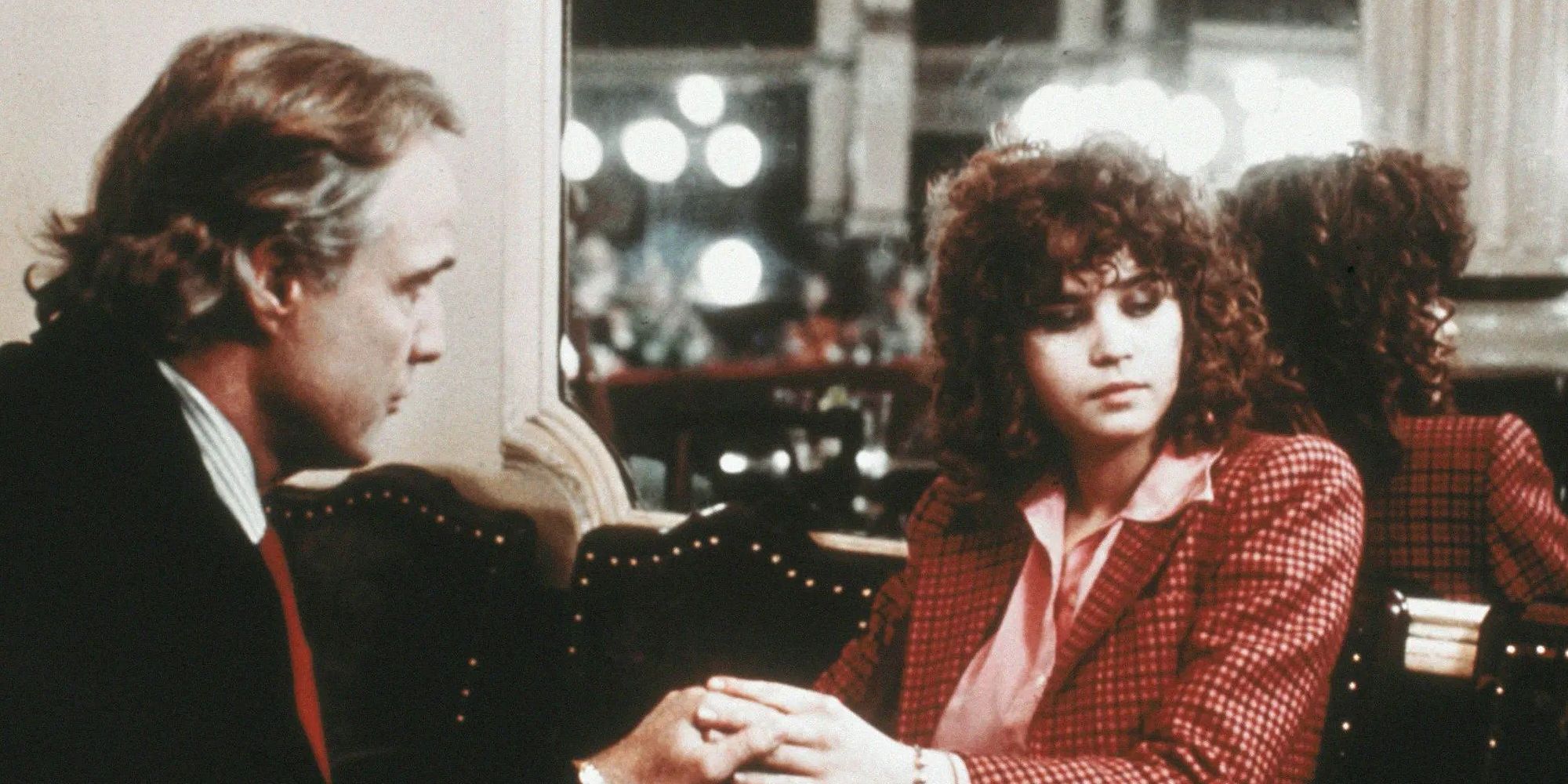 Marlon Brando as Paul and Maria Schneider as Jeanne hold hands and sit in a lobby in Last Tango in Paris.