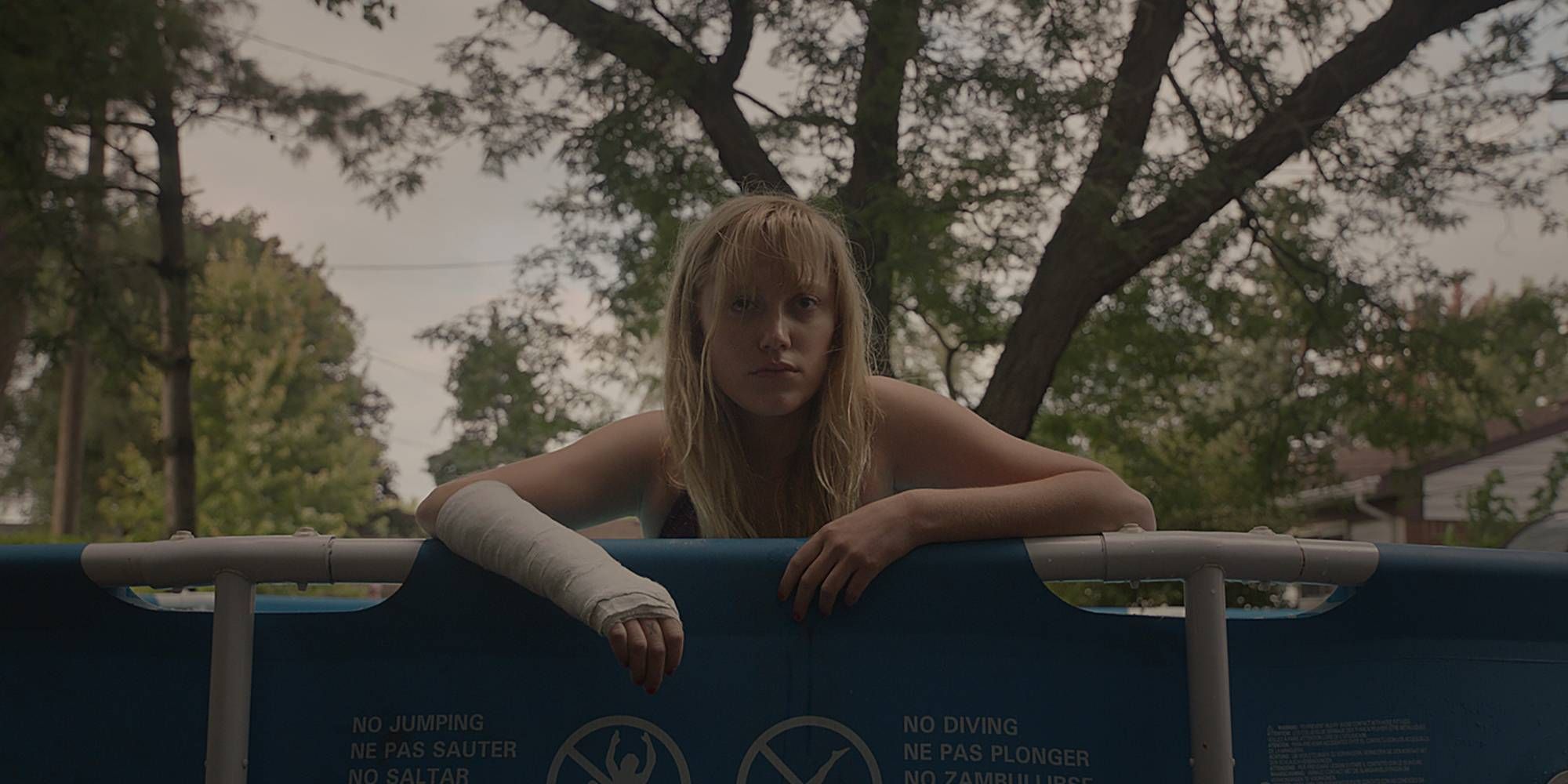Maika Monroe with an arm cast leans over the edge of pool in It Follows