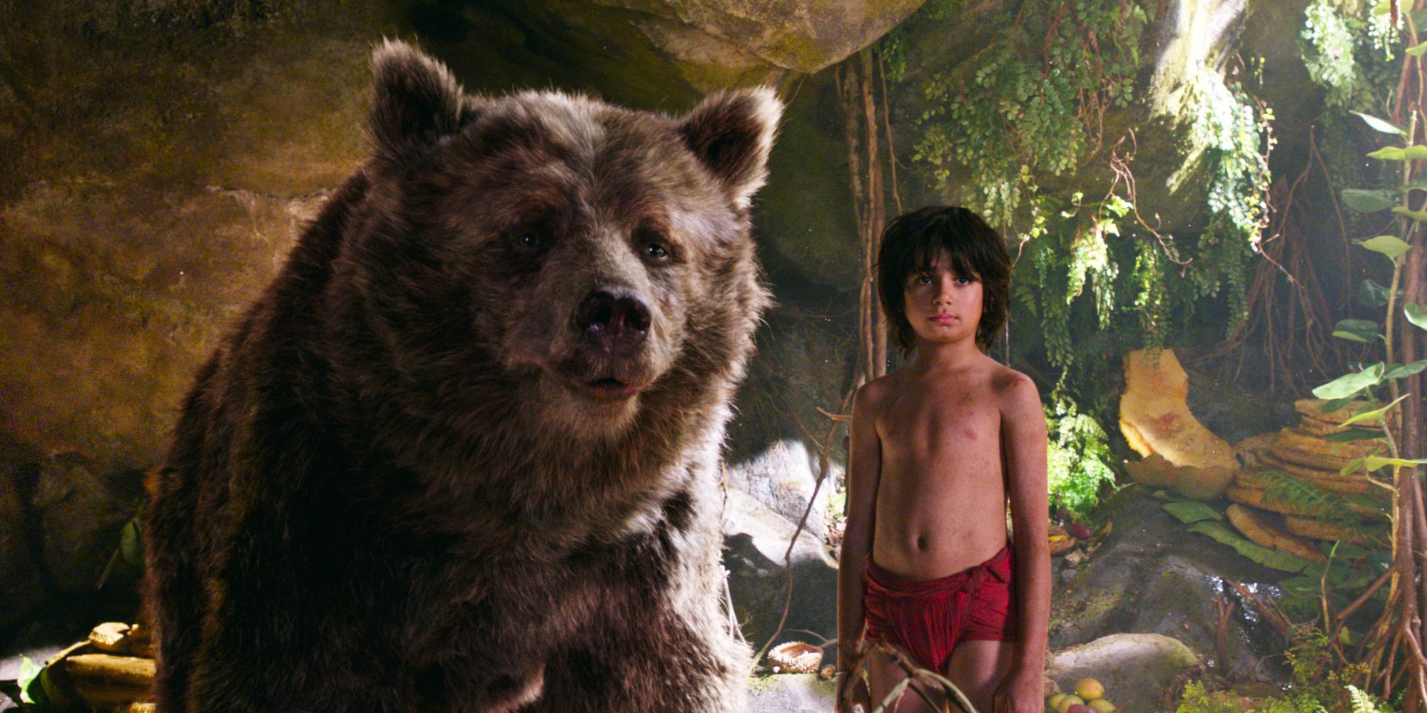 Neel Sethi as Mogli standing next to a bear in The Jungle Book.