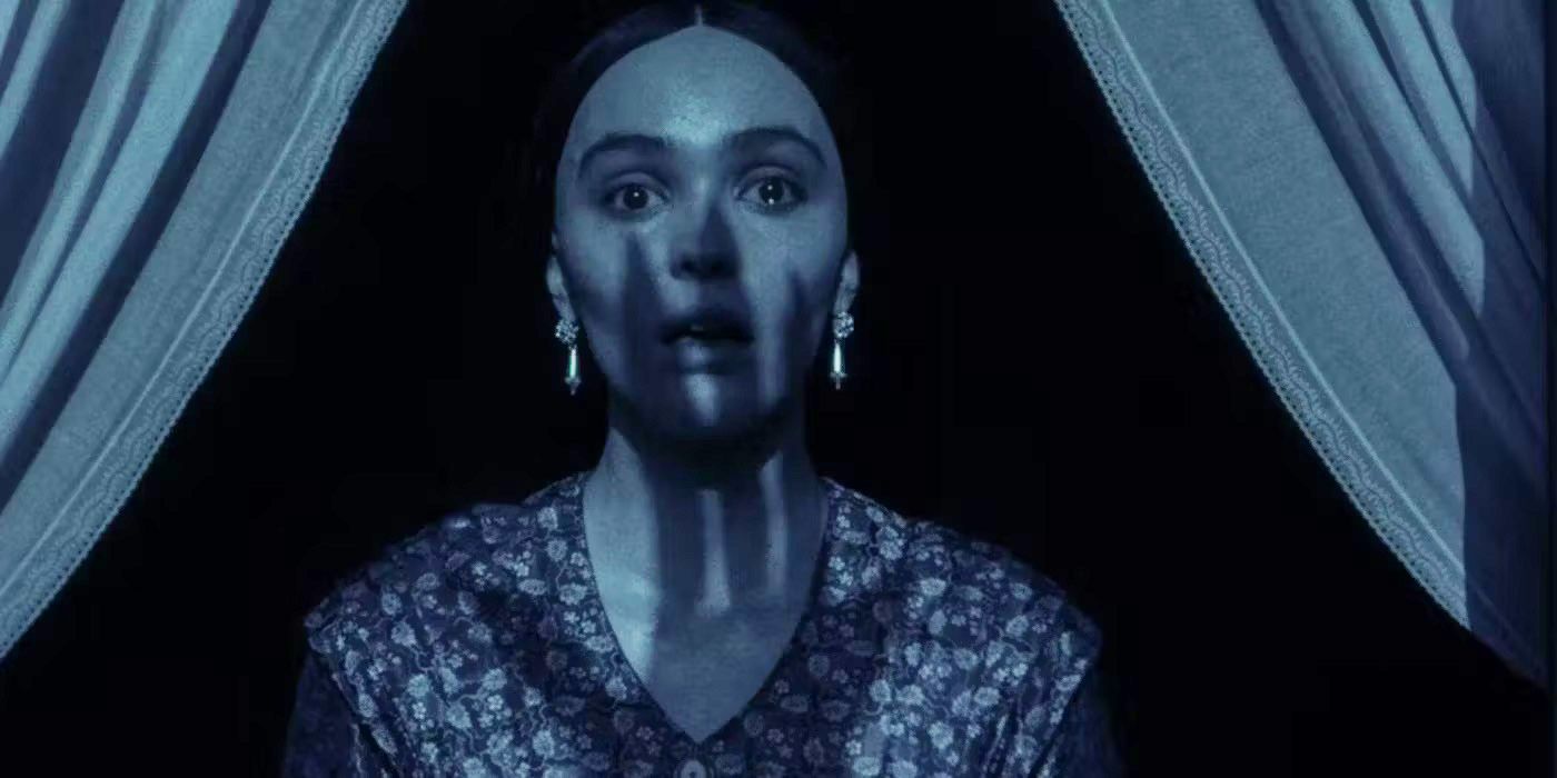 Lily Rose Depp in Robert Eggers Nosferatu remake as Ellen Hutter looking out a moonlit window with the shadow of a long terrifying hand on her face