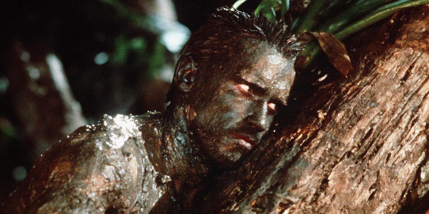 Arnold Schwarzenegger coberto de lama e apoiando -se em um tronco de árvore em Predator