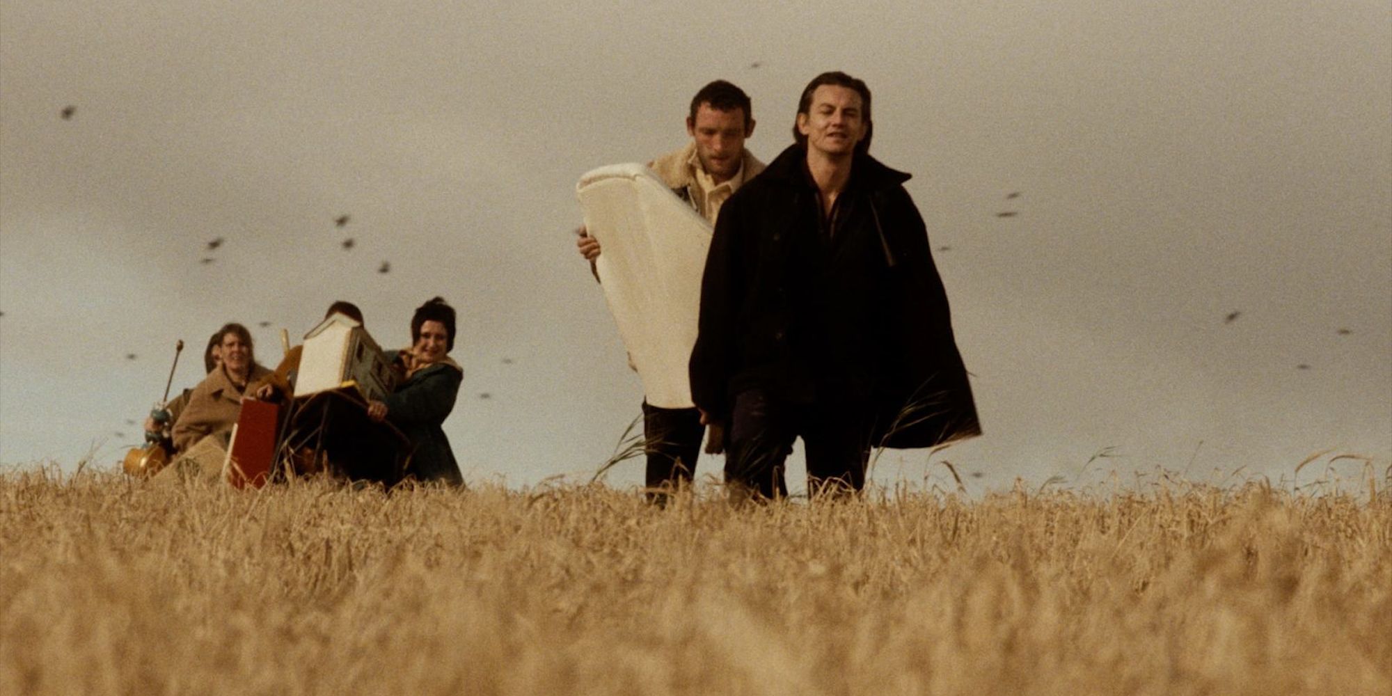 man in black coat walking in a field with men behind him.