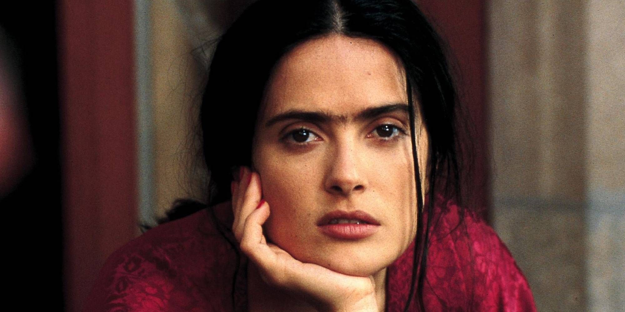 Salma Hayek as Frida Kahlo staring at the camera while resting her chin on her hand in the film Frida.