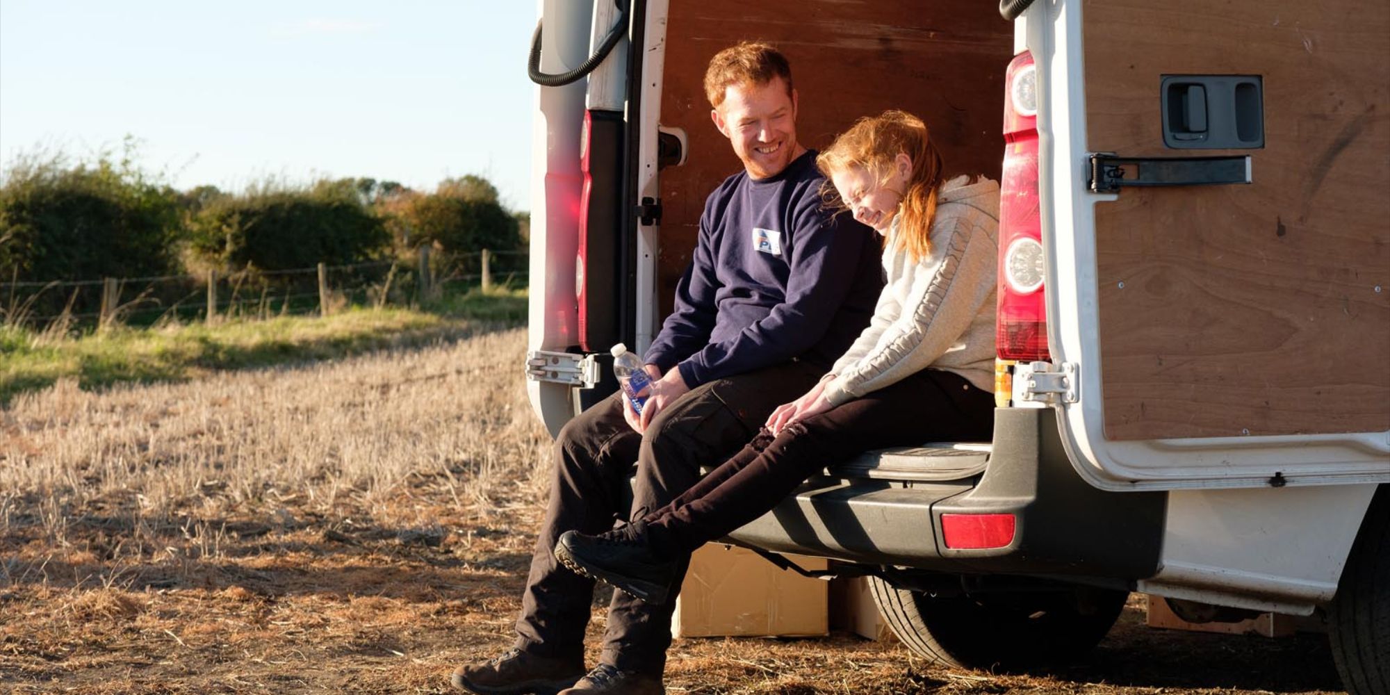 Pai e filha sentados na traseira de uma van em Desculpe, sentimos sua falta