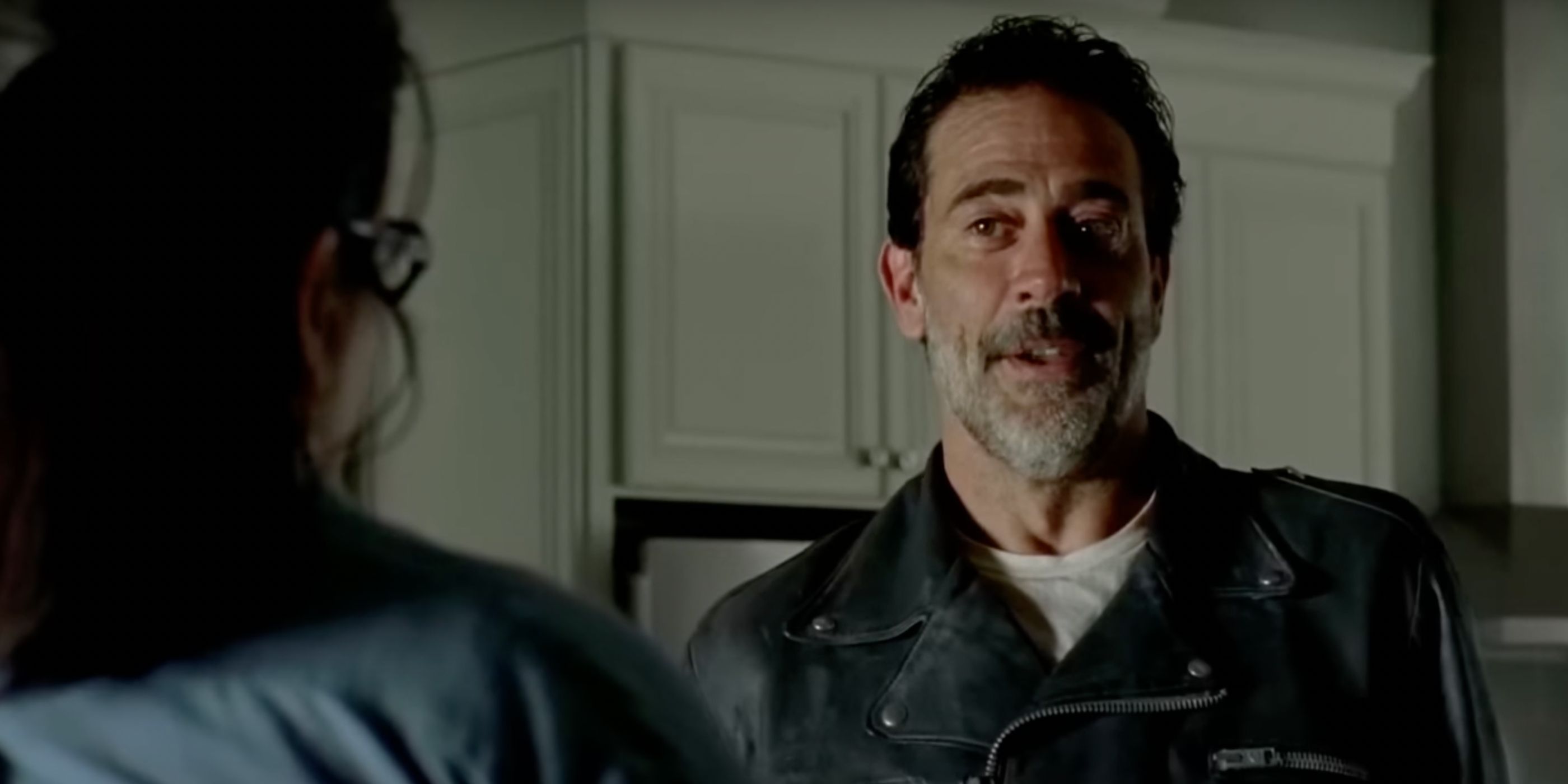 Negan (Jeffrey Dean Morgan) stands in a house in Alexandria, sporting a cruel smile as he taunts Olivia (Ann Mahoney)