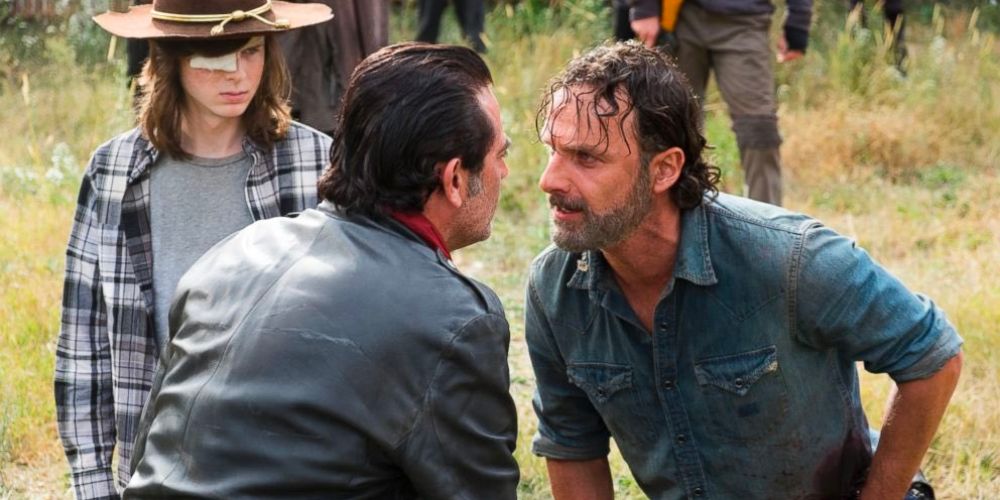 Rick and Negan confront each other in a grassy field with Carl standing by while they're surrounded by armed men.