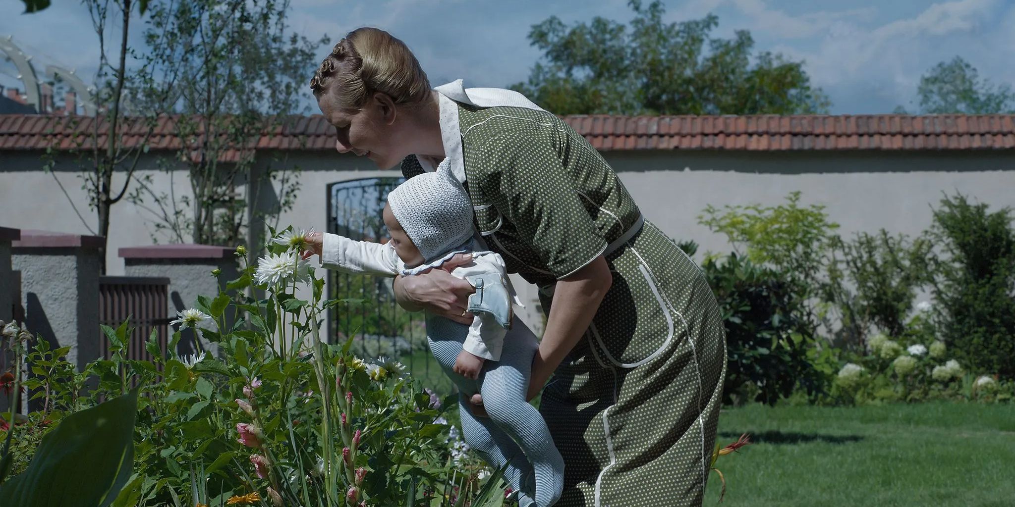 In ‘The Zone of Interest’, Höss’s wife played by Sandra Hüller picks flowers in her garden with her baby.