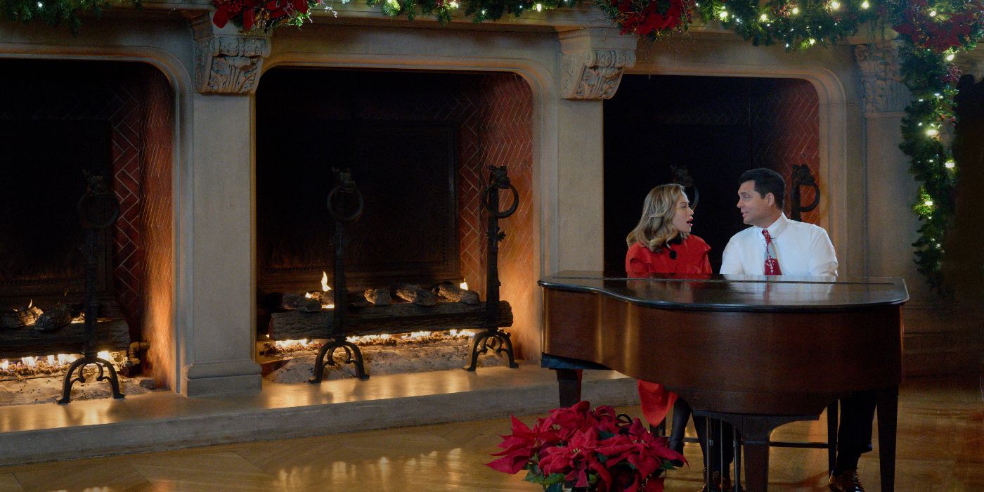 A wide shot of Bethany Joy Lutz&rsquo;s Lucy and Kristoffer Polaha&rsquo;s Jack singing together at a grand piano with fireplaces behind them and lighted Christmas garland in Hallmark&rsquo;s A Biltmore Christmas