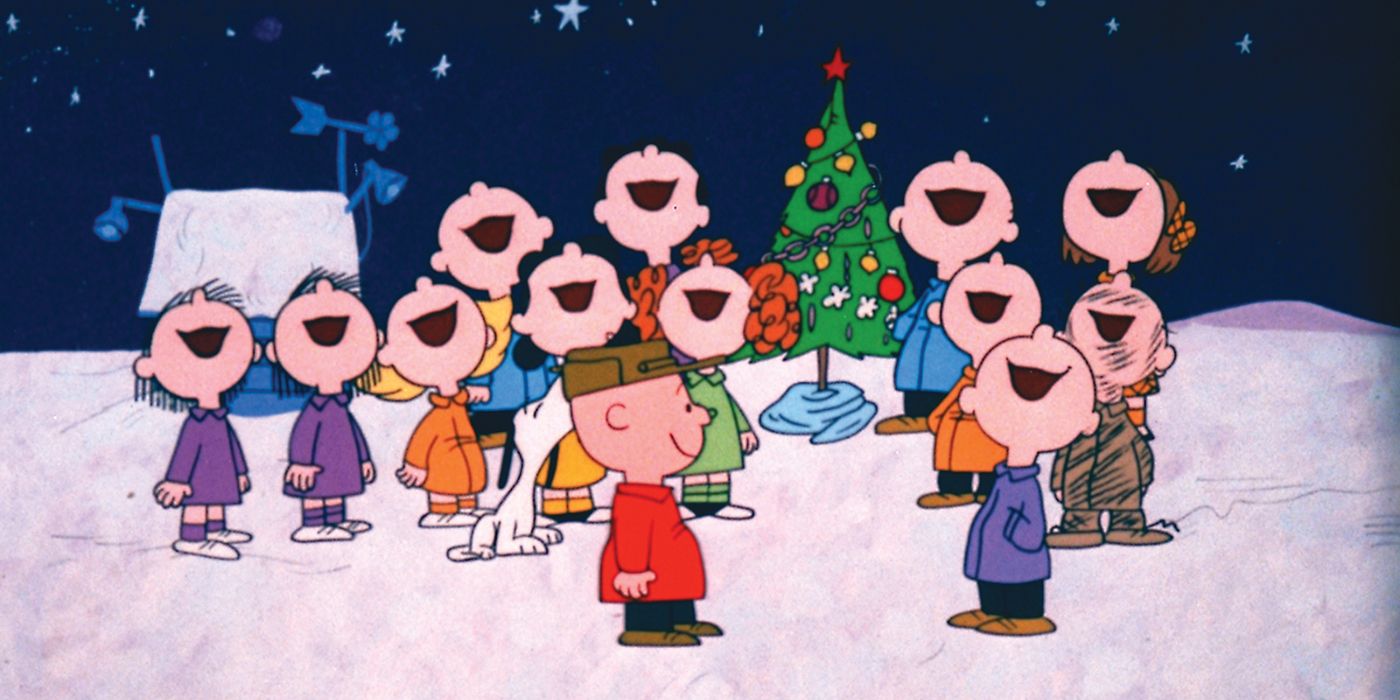 The Peanuts singing as a group in front of a beautifully decorated little Christmas tree while Charlie Brown smiles in A Charlie Brown Christmas