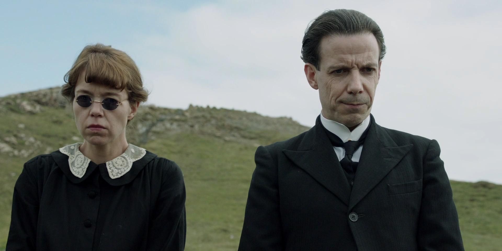 Anna Maxwell Martin and Noah Taylor as Mrs. and Mr. Rogers standing outside with green island hills behind them in And Then There Were None