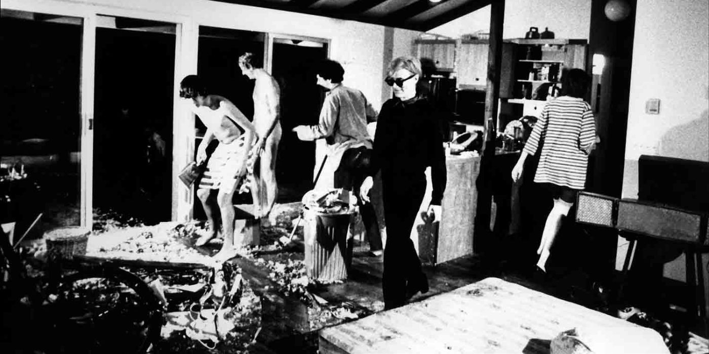 Andy Warhol walking through a room with shirtless men on the backgroun in Four Stars 1