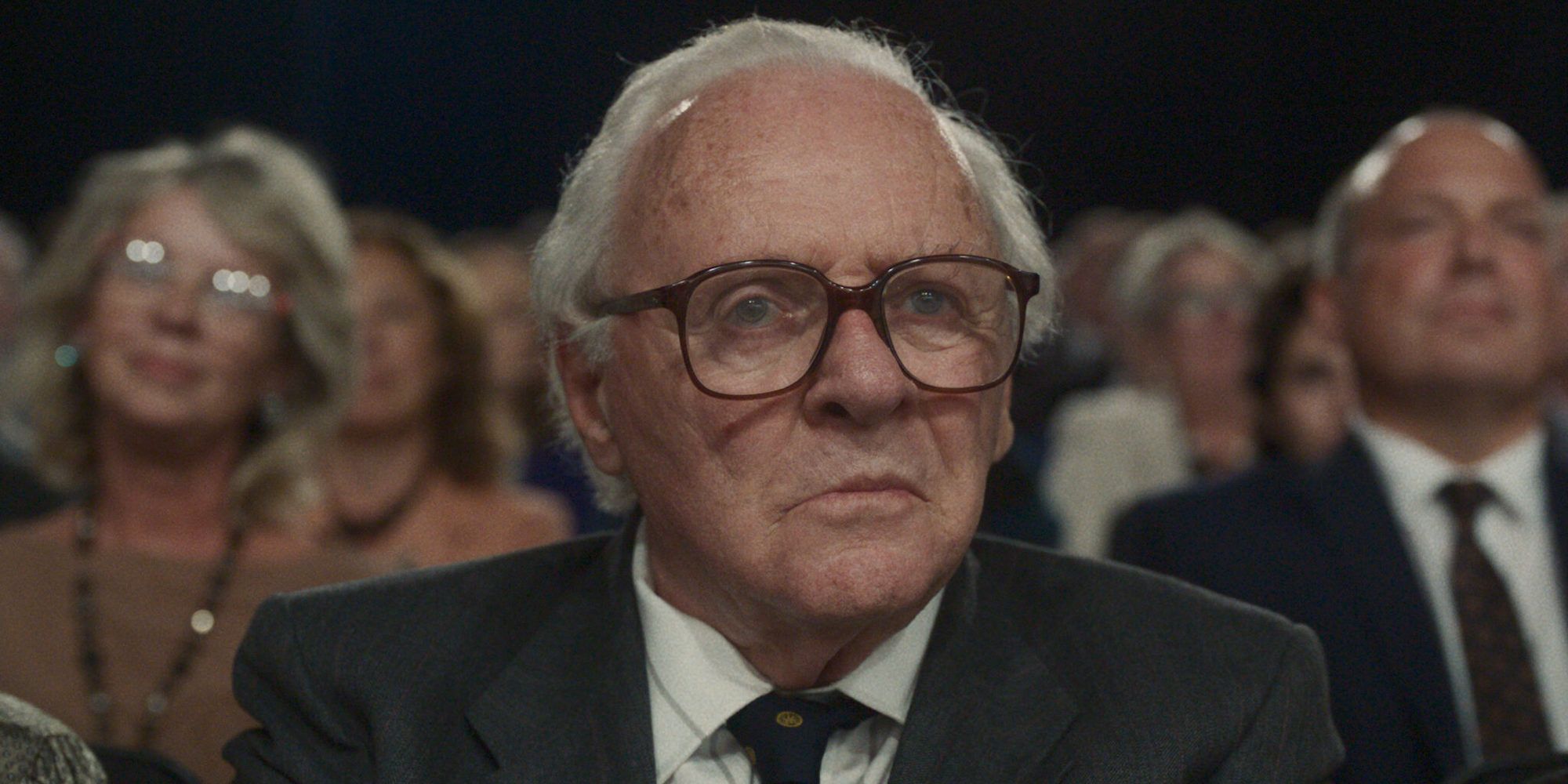 Anthony Hopkins, playing Nicholas Winton, sitting in a crowd with glasses on