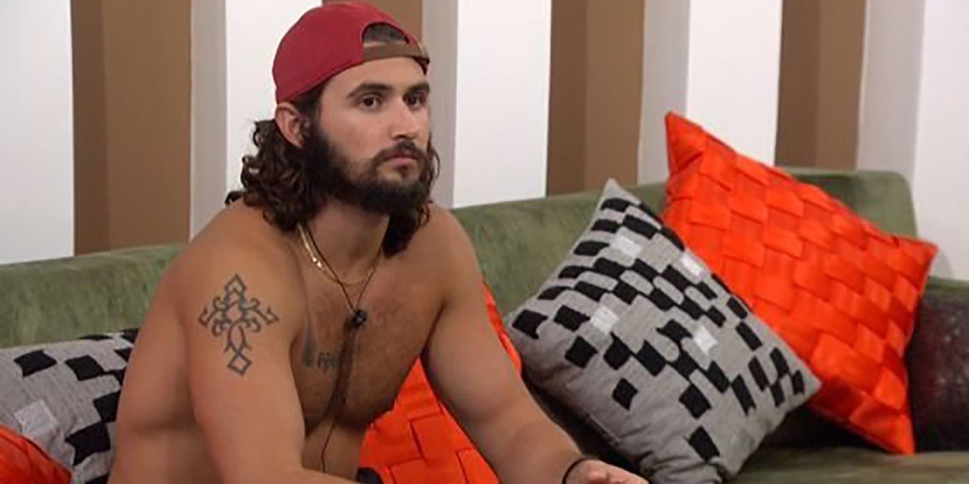 Victor Arroyo sitting on the couch in Big Brother wearing a hat backwards and looking upset.