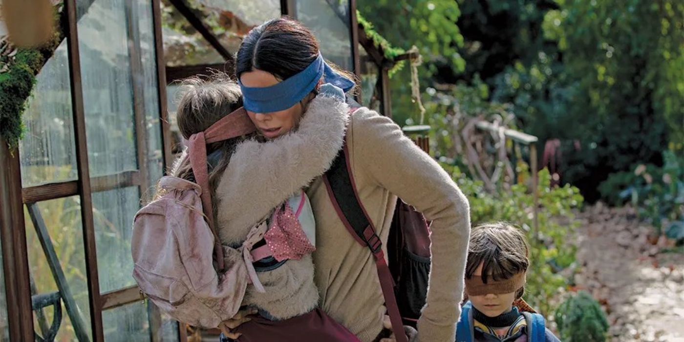 Sandra Bullock como Malorie vendada carregando uma criança em Bird Box