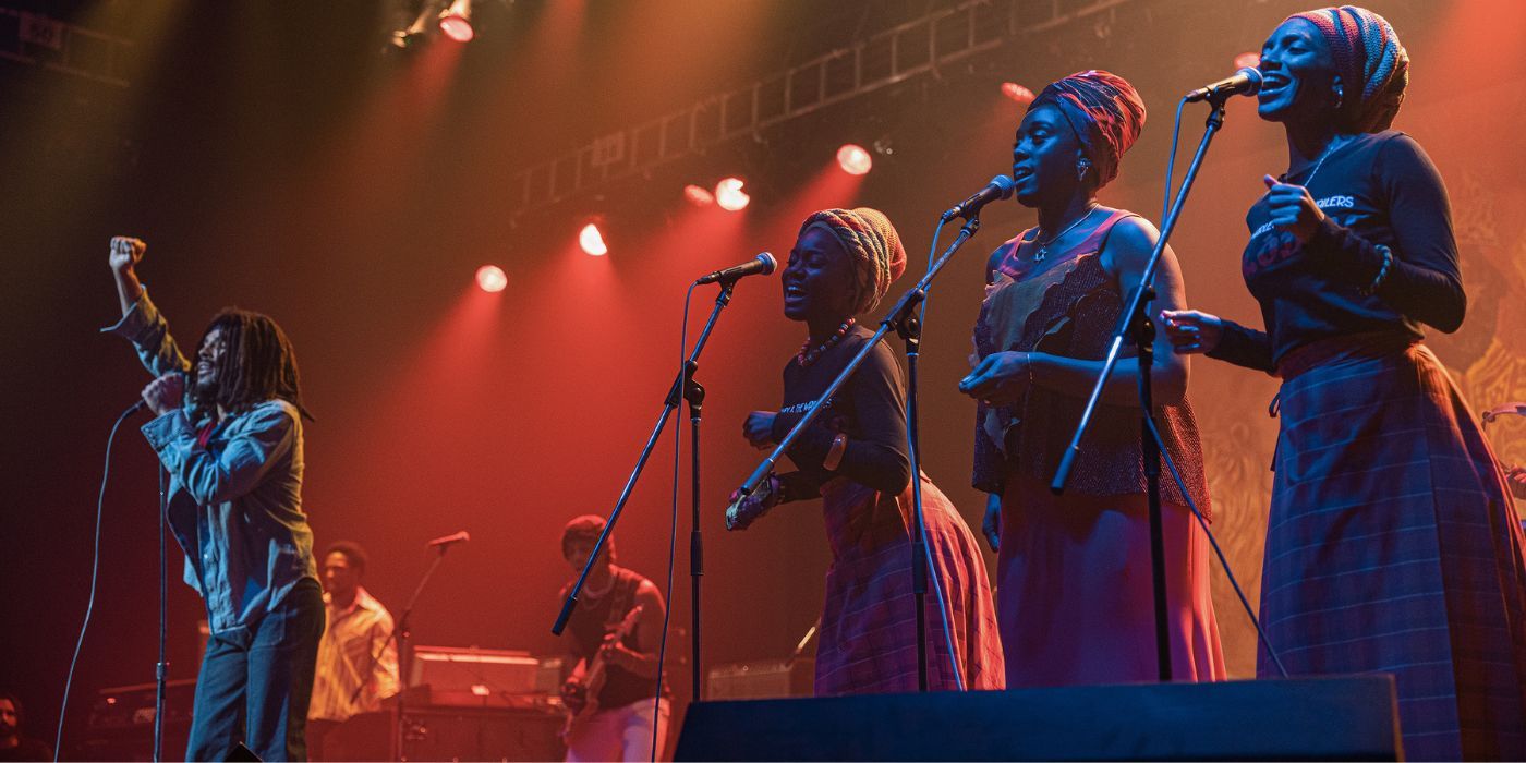 Bob Marley (Kingsley Ben-Adir) singing on stage while accompanied by Judy Mowatt (Anna-Sharé Blake), Rita Marley (Lashana Lynch), and Marcia Griffiths (Naomi Cowan).