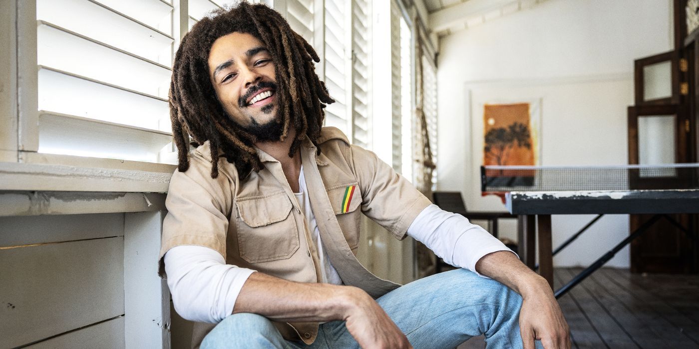 Kingsley Ben-Adir as Bob Marley smiling while sitting in the biopic Bob Marley: One Love