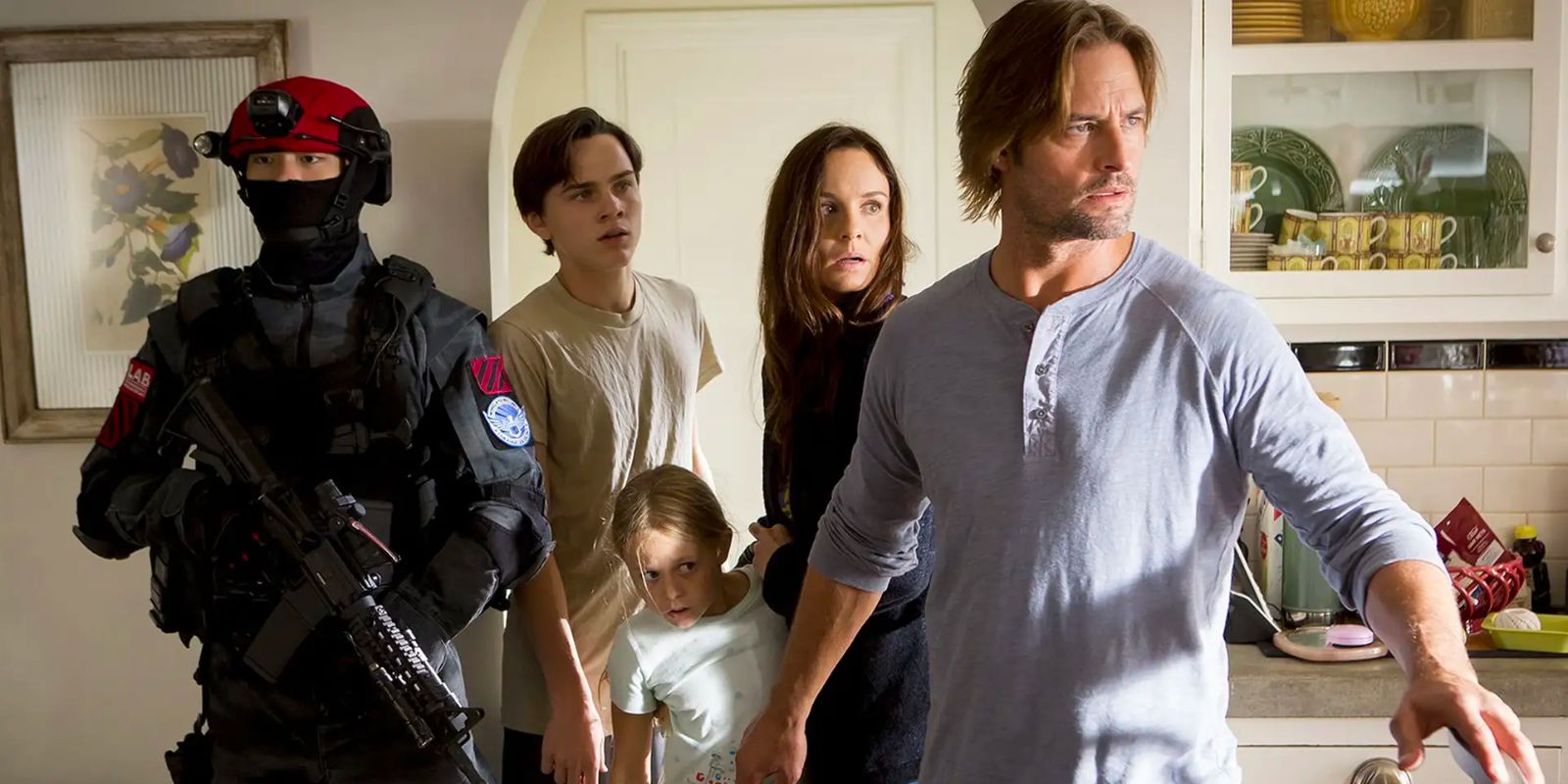 A family walks through the halls of a nice, suburban house while an armed soldier stands guard in the walkway.