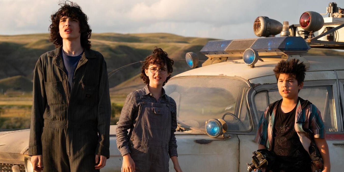Finn Wolfhard, McKenna Grace, and Logan Kim stand in front the ectomobile in 'Ghostbusters Afterlife' (2021)