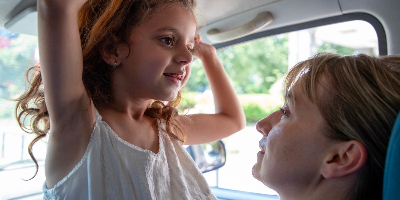 A young girl laughs in the arms of an older woman in a car in Housekeeping for Beginners 