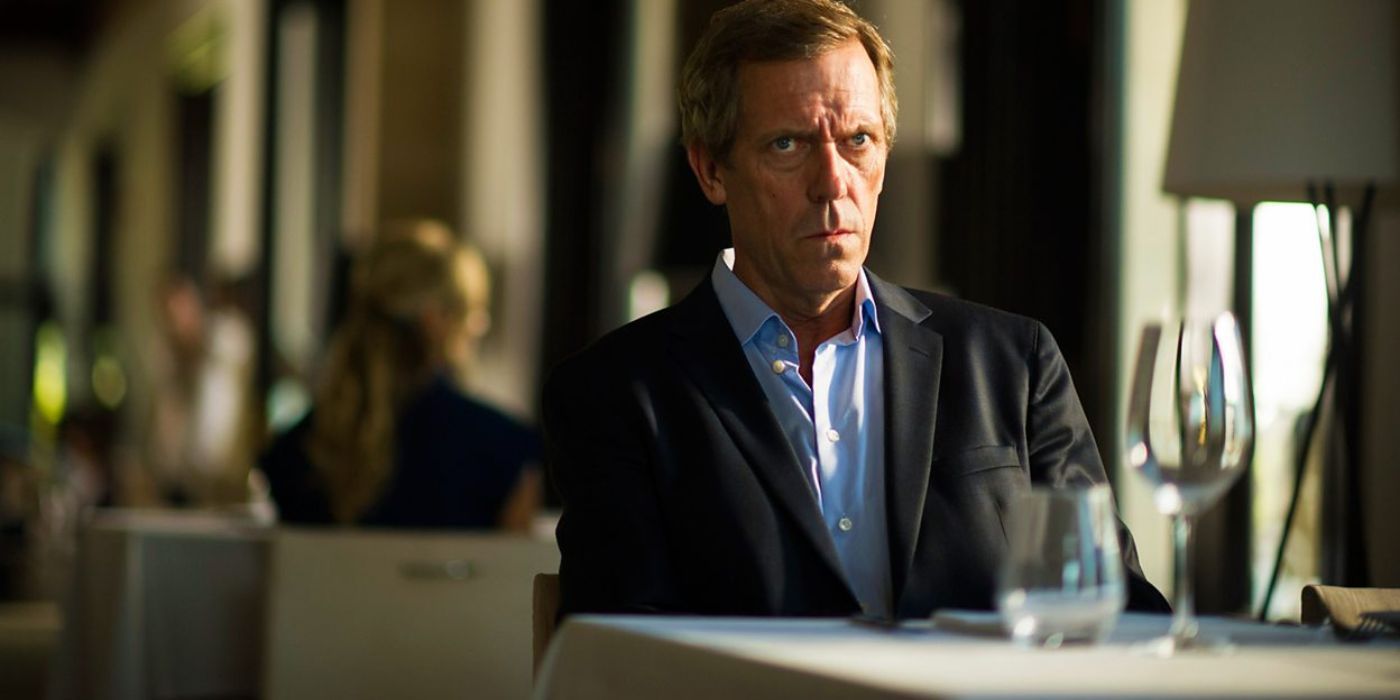 Hugh Laurie as Richard Roper seated at a restaurant table looking serious in the miniseries,  'The Night Manager'
