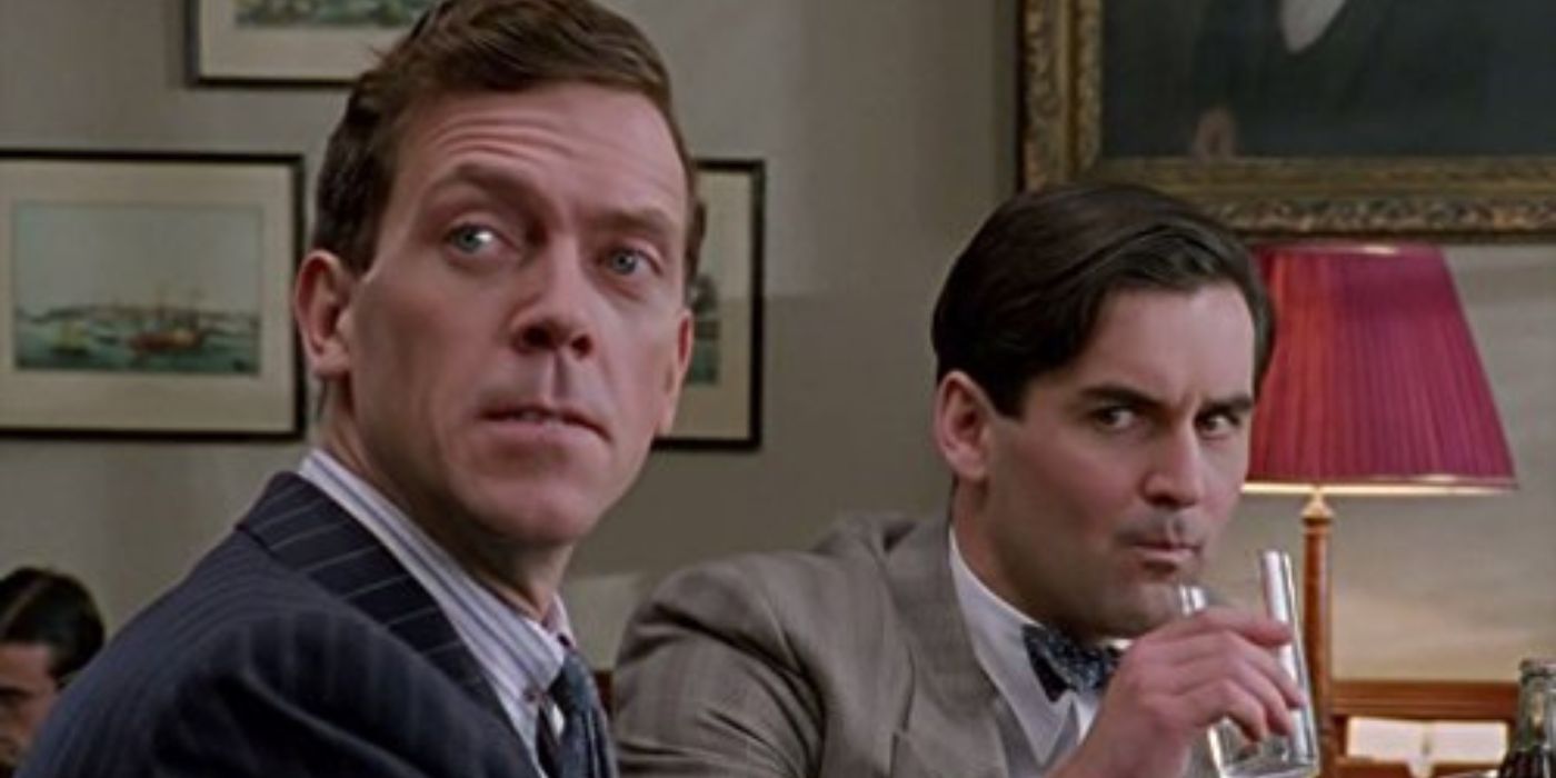 Hugh Laurie as Bertie Wooster is looking over his shoulder while a man behind him sips a drink