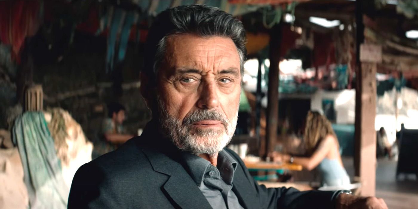 Ian McShane as Wilson, sitting and looking at a person offscreen, in American Star
