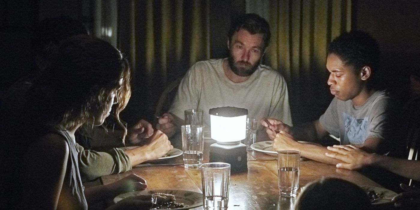 três pessoas sentadas em uma mesa ao redor de uma luminária em It Comes at Night 