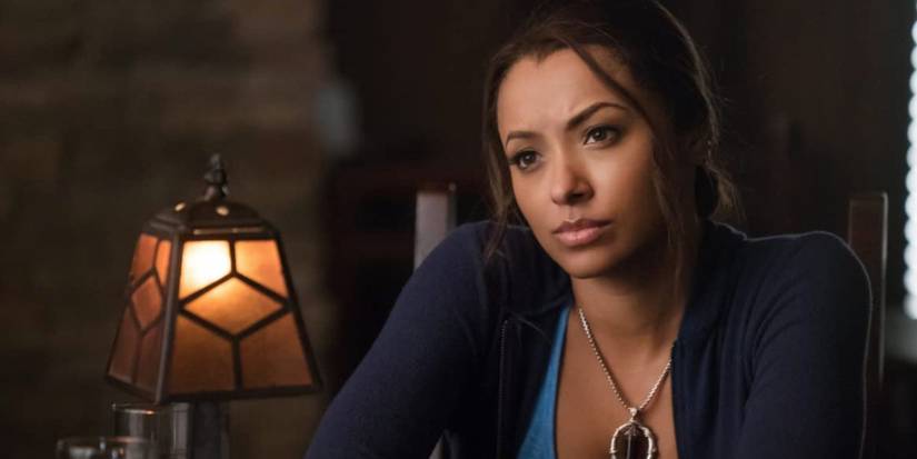Kat Graham as Bonnie Bennett with an arched eyebrow sitting at a table in The Vampire Diaries.