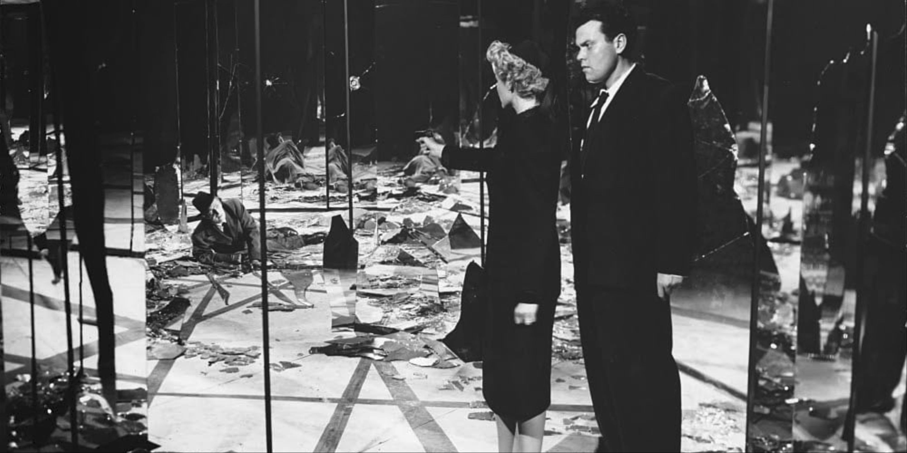 Rita Hayworth as Elsa Bannister pointing a gun at a man as Orson Welles as Michael O'Hara stands behind her in The Lady from Shanghai