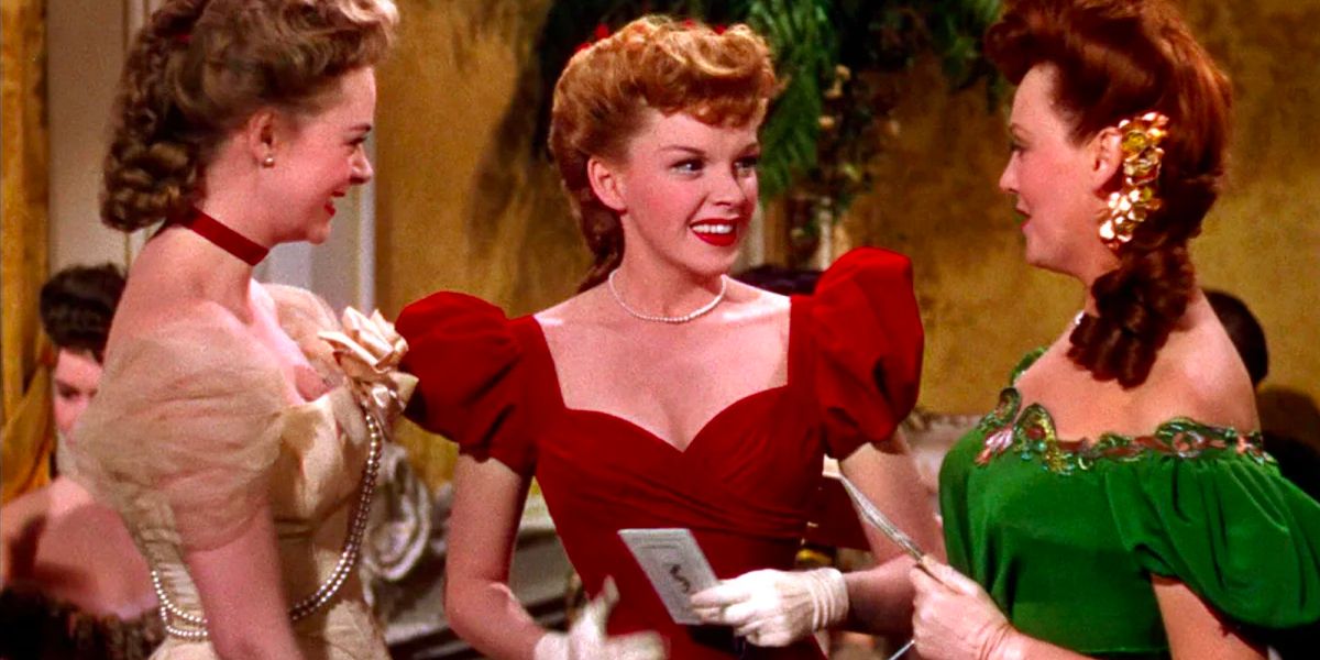 Three young women wearing festive dresses smile and talk at a Christmas party. 