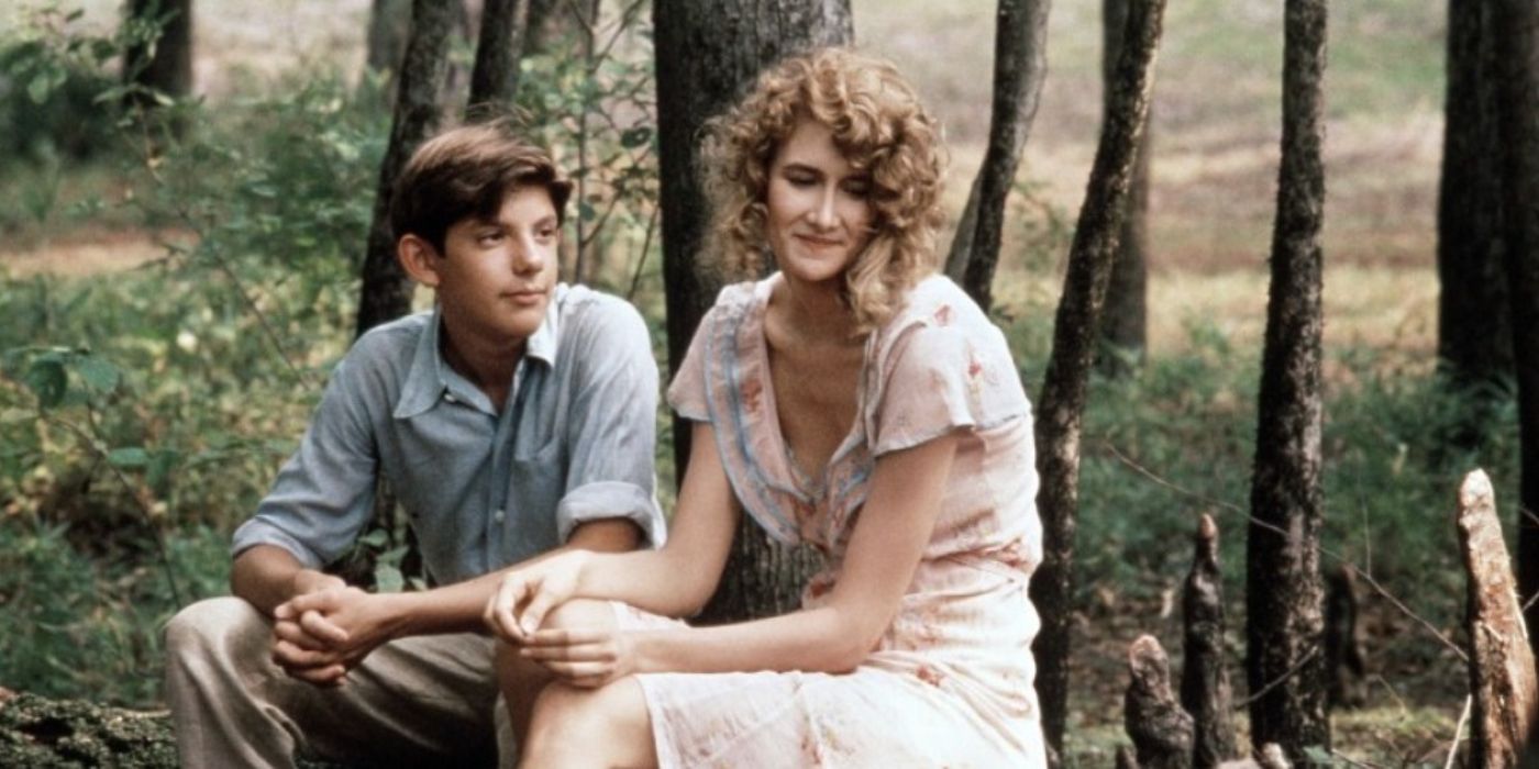 Lukas Haas looks at Laura Dern as she looks away as they sit together in a forest in Rambling Rose.