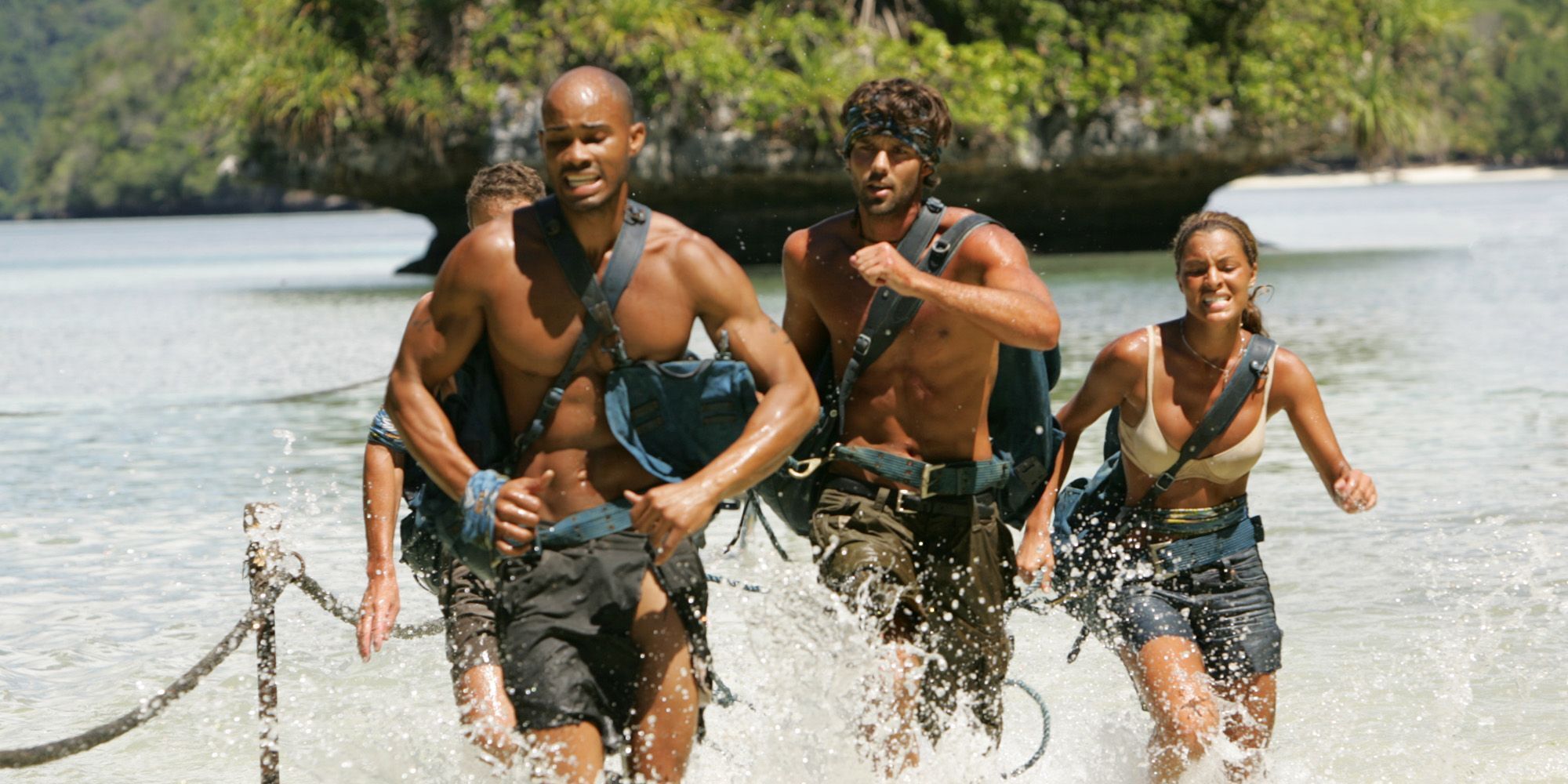 A still from the 10th season of Survivor, Palau, featuring the Ulong tribe competing in a challenge as they run through shallow waters carrying heavy weighted bags